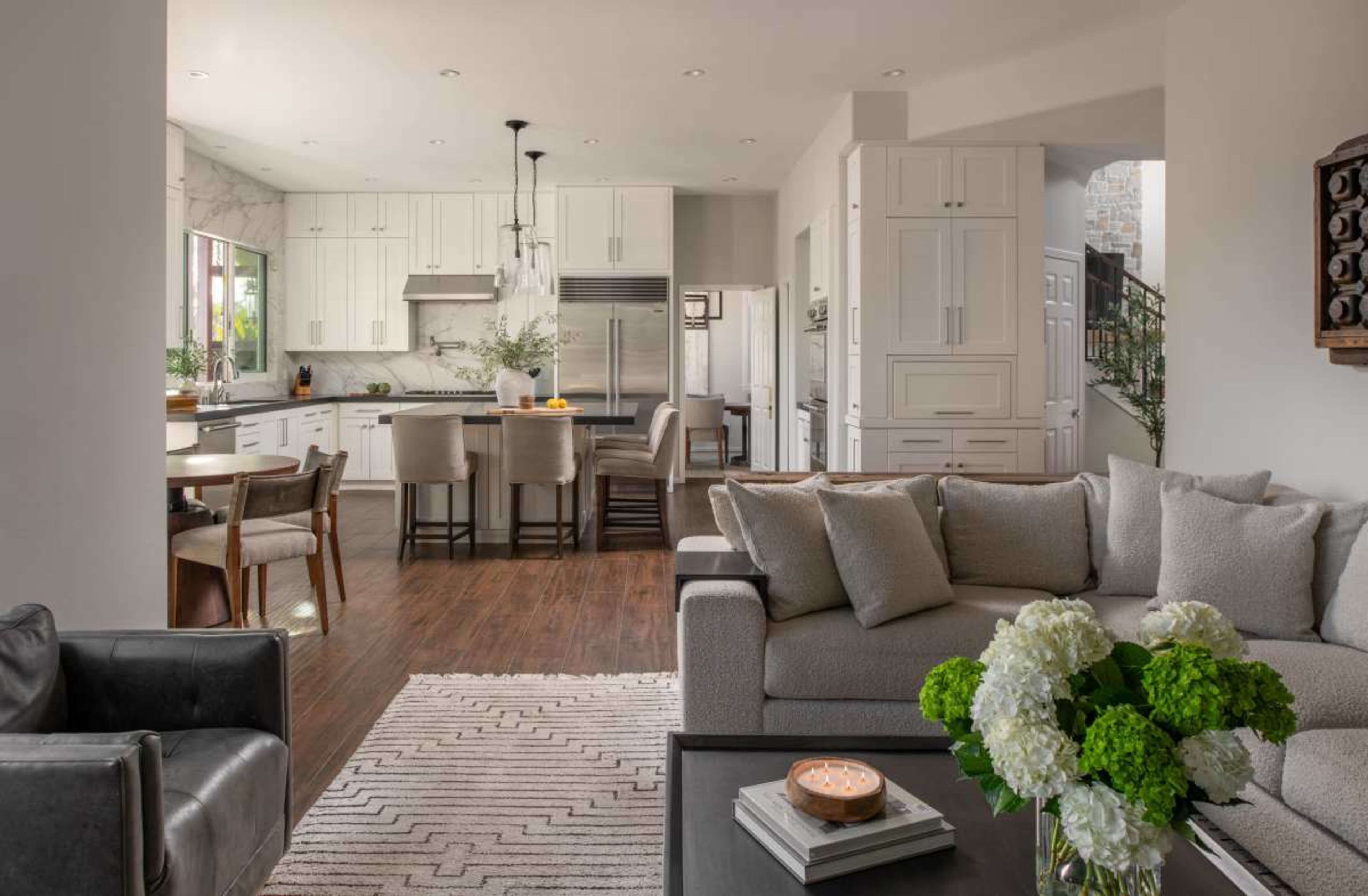 The image shows a modern kitchen and living room area with light-colored cabinetry, a large kitchen island, and a sofa arranged around a coffee table.