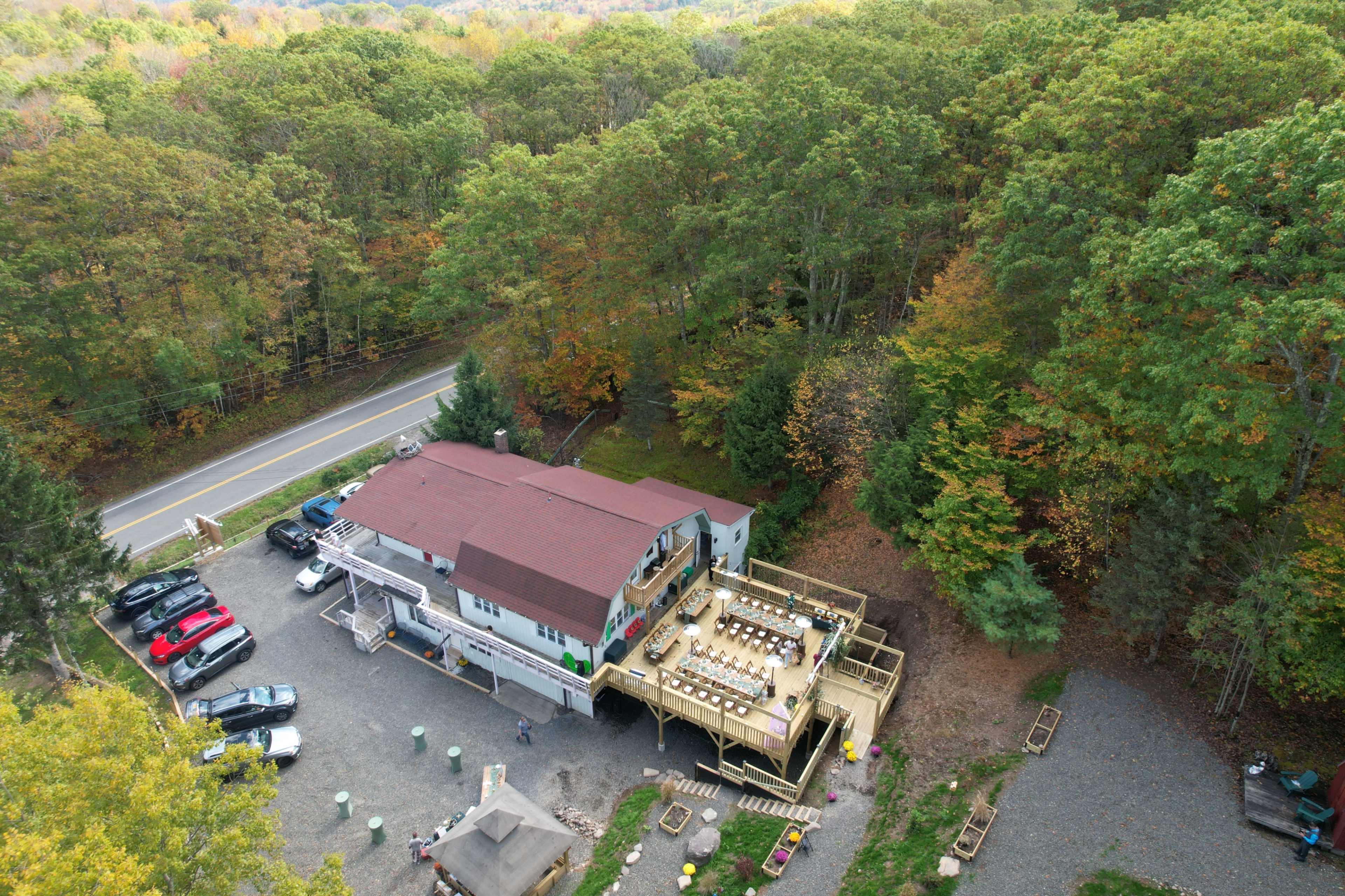 The image shows a two-story building with a large deck situated near a road, surrounded by trees with autumn foliage.