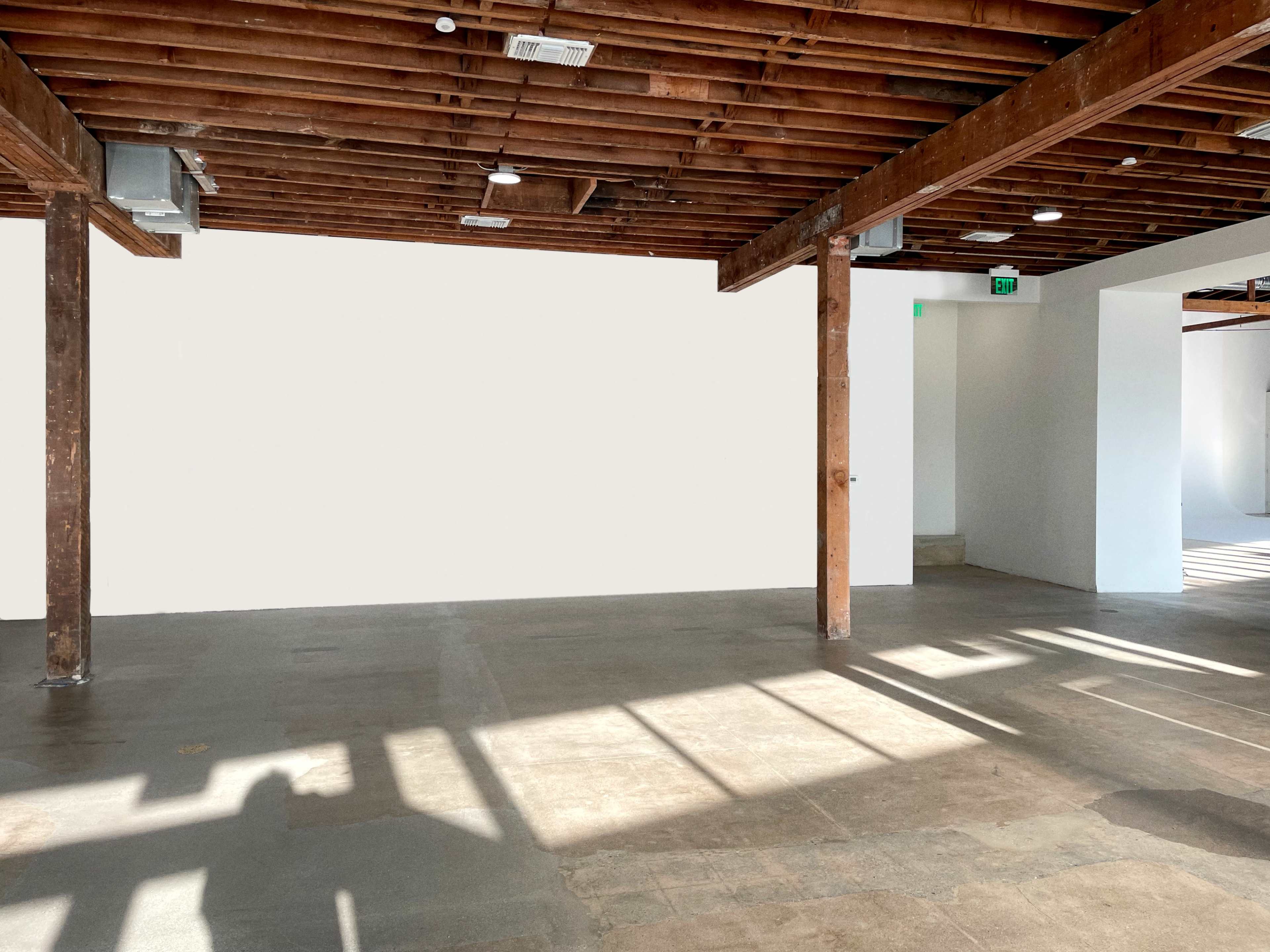 A spacious interior with exposed wooden beams, a light-colored wall, and a tiled floor.