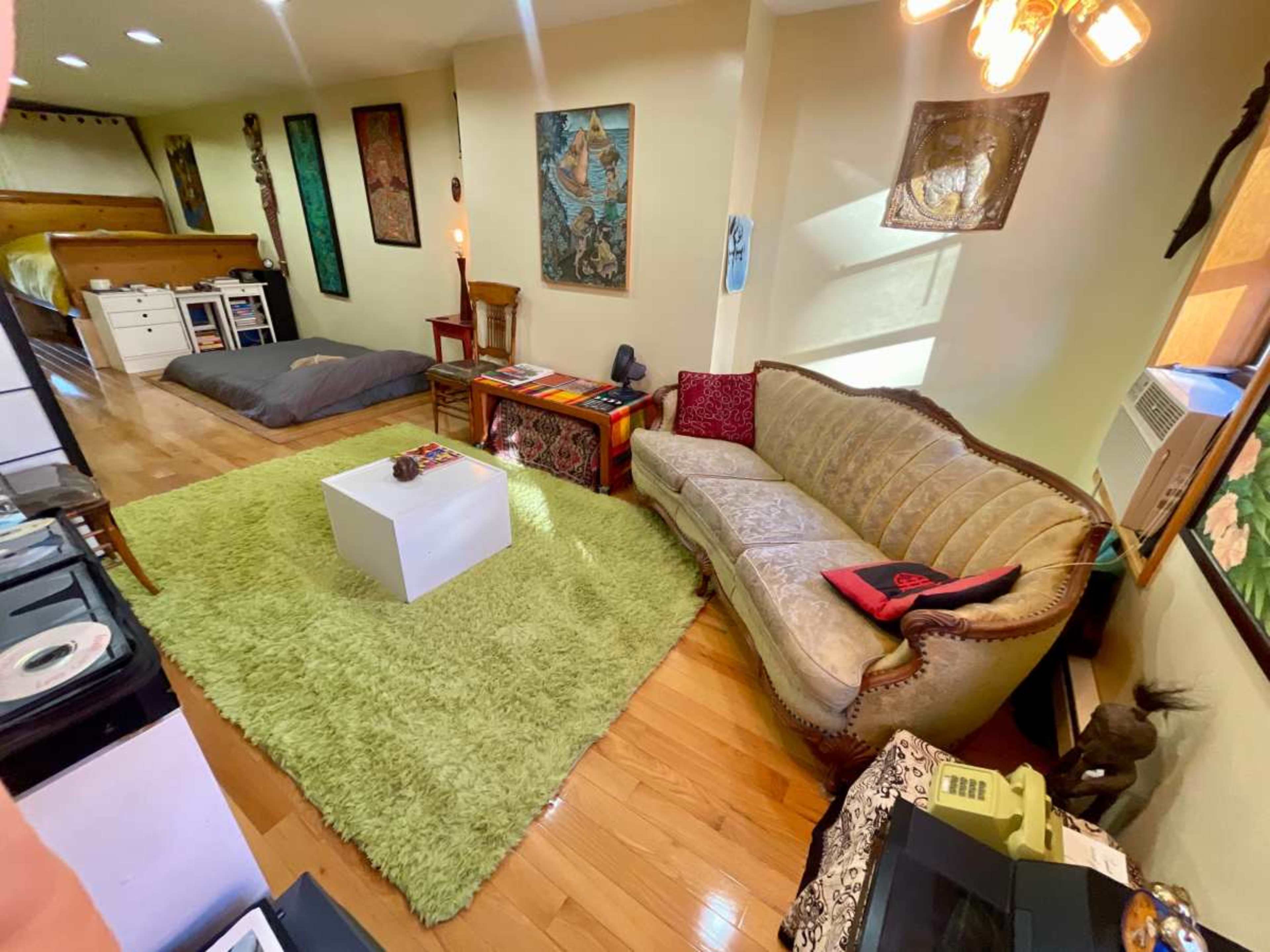 The image shows a living space featuring a green rug, a white table, a vintage sofa, and various wall decorations.