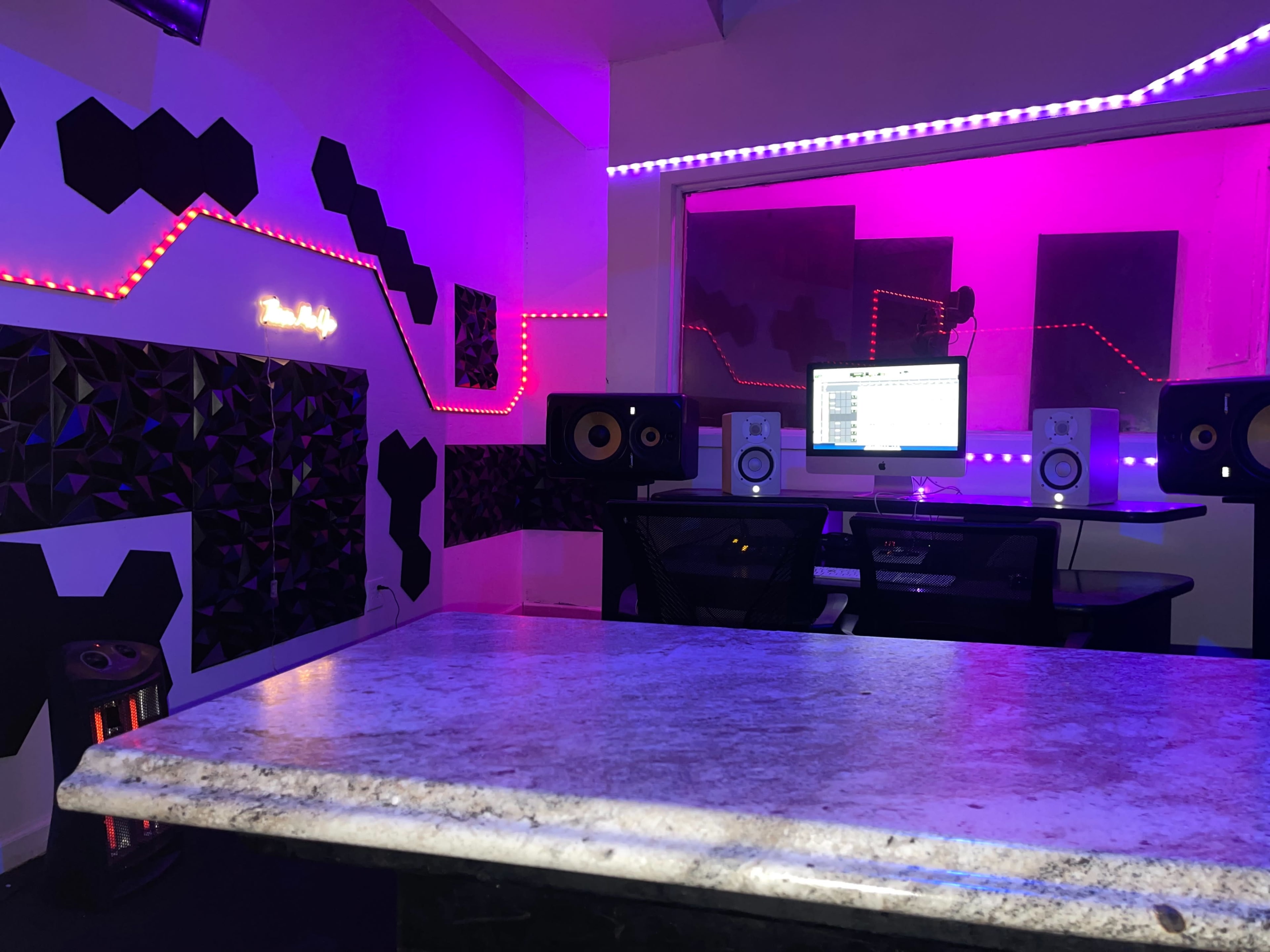 A modern music studio with a mixing desk, speakers, and colorful LED lighting on the walls.