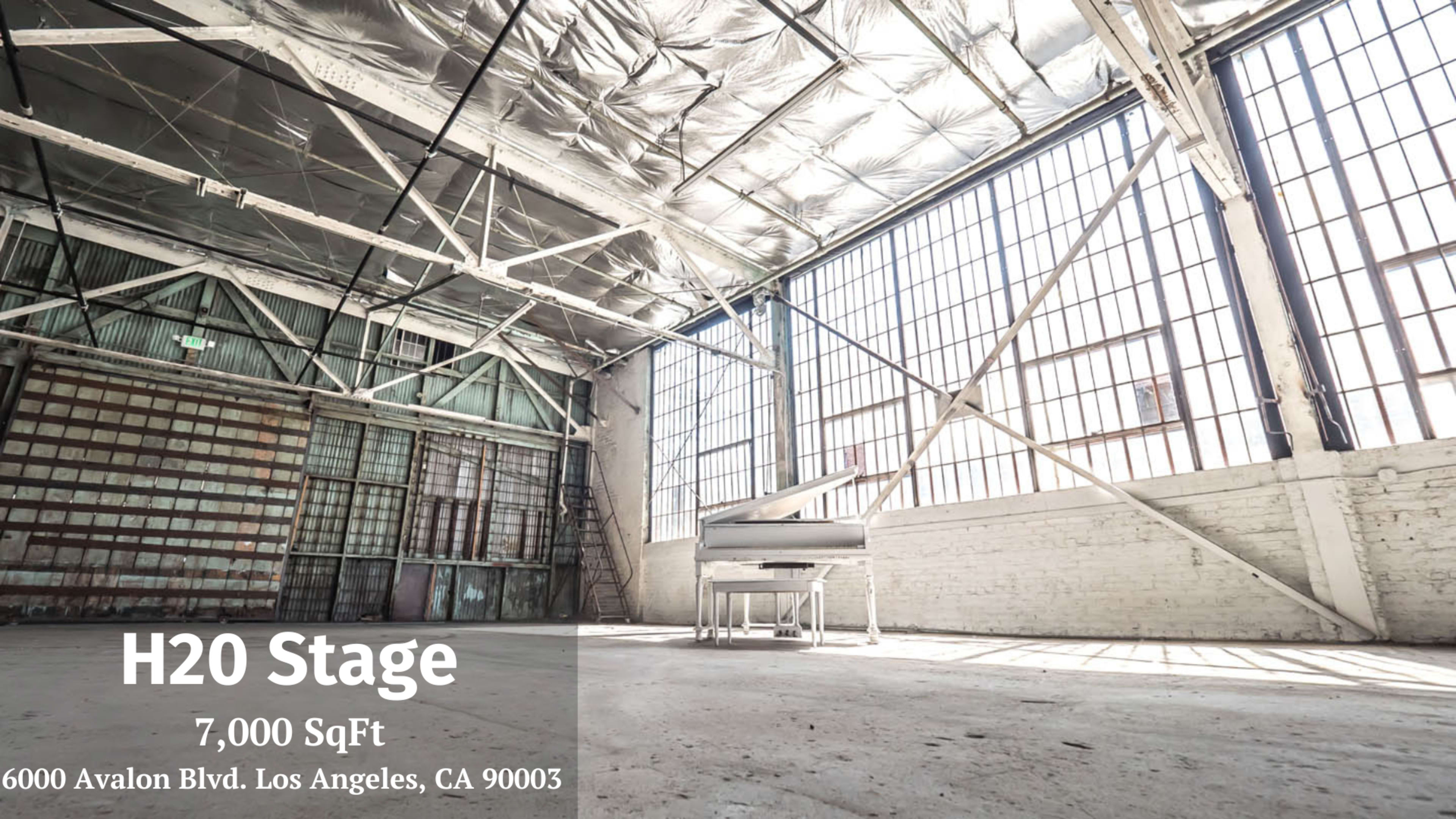The image shows a spacious industrial venue with large windows and exposed beams, featuring a piano in one corner.