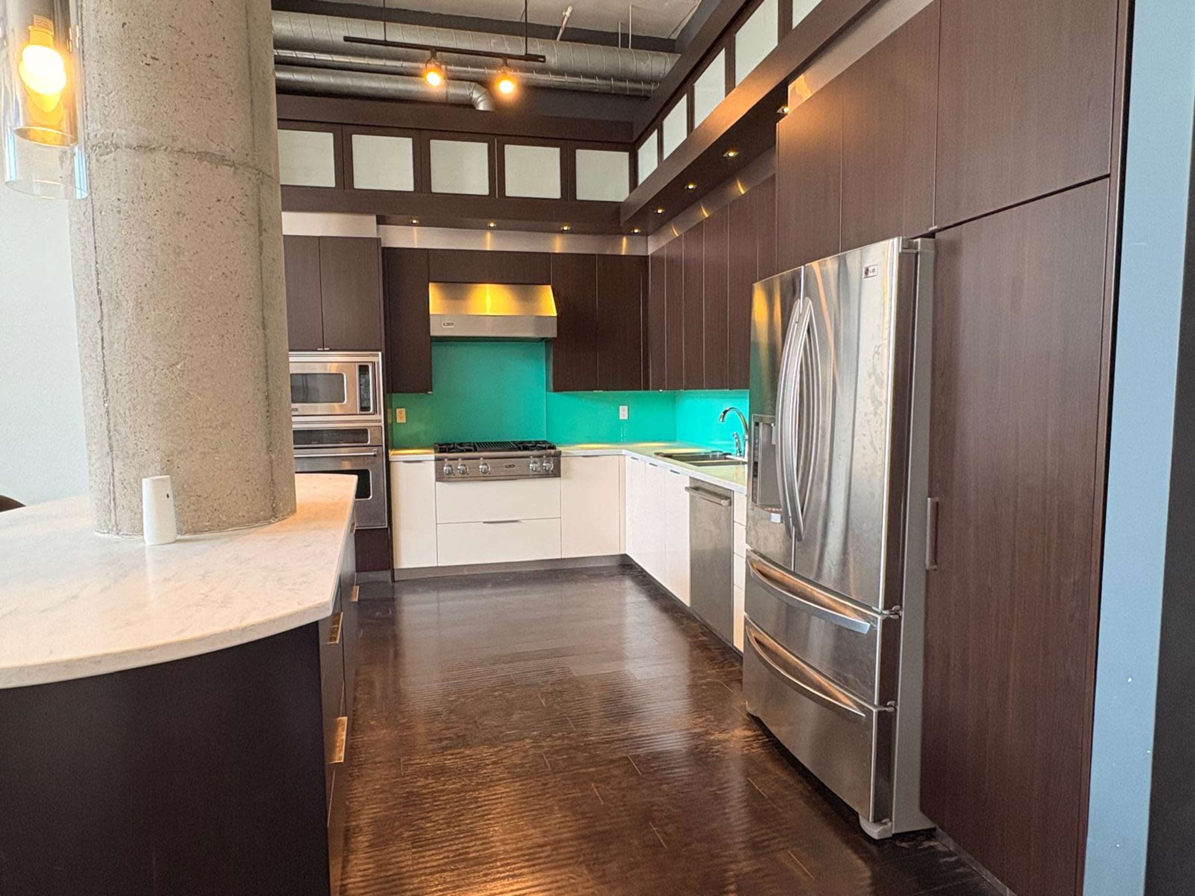 The image shows a modern kitchen with dark cabinetry, a contrasting turquoise backsplash, stainless steel appliances, and a marble countertop.