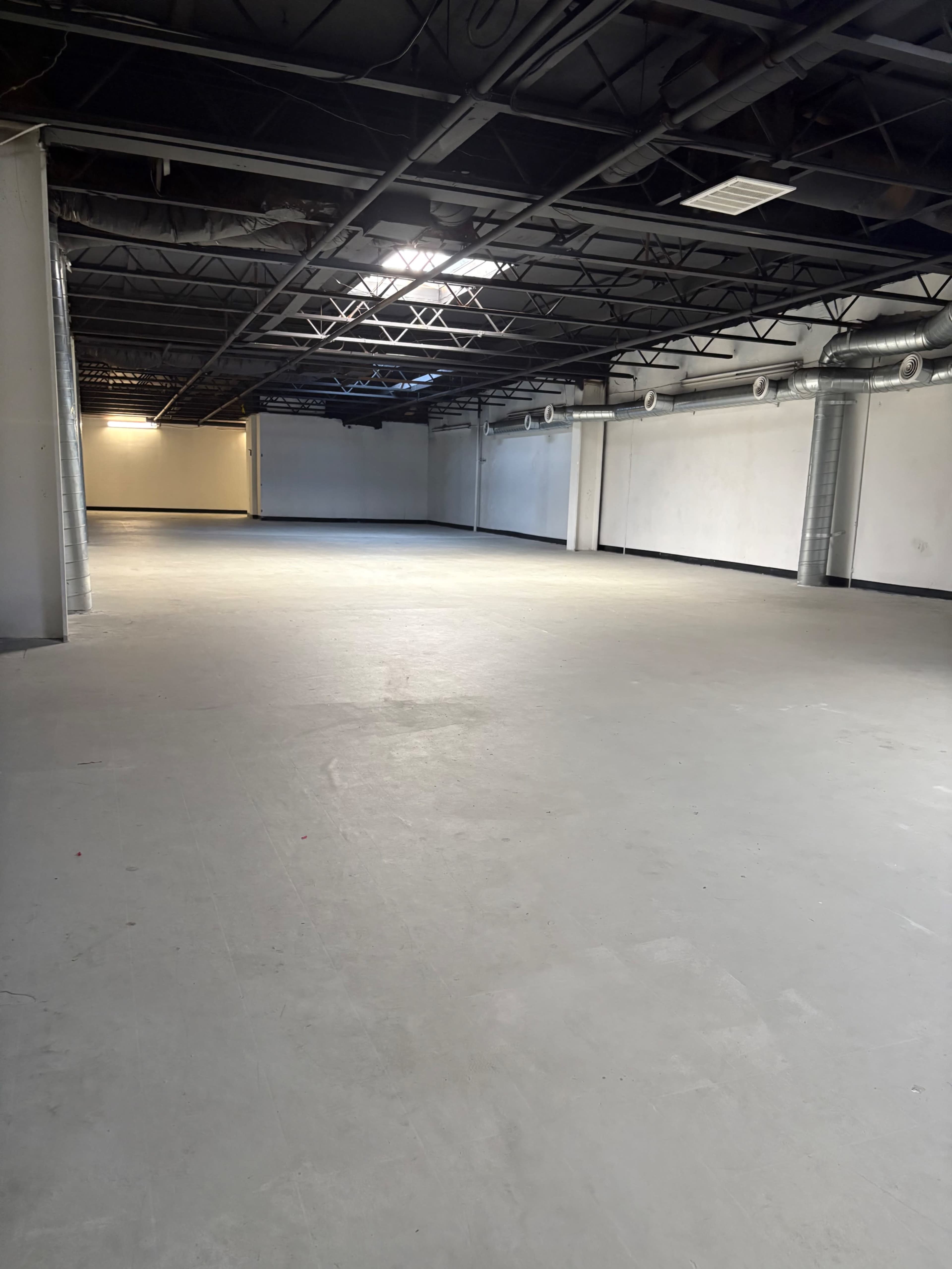 The image shows a large, empty industrial space with a concrete floor, high ceilings, and exposed ductwork.