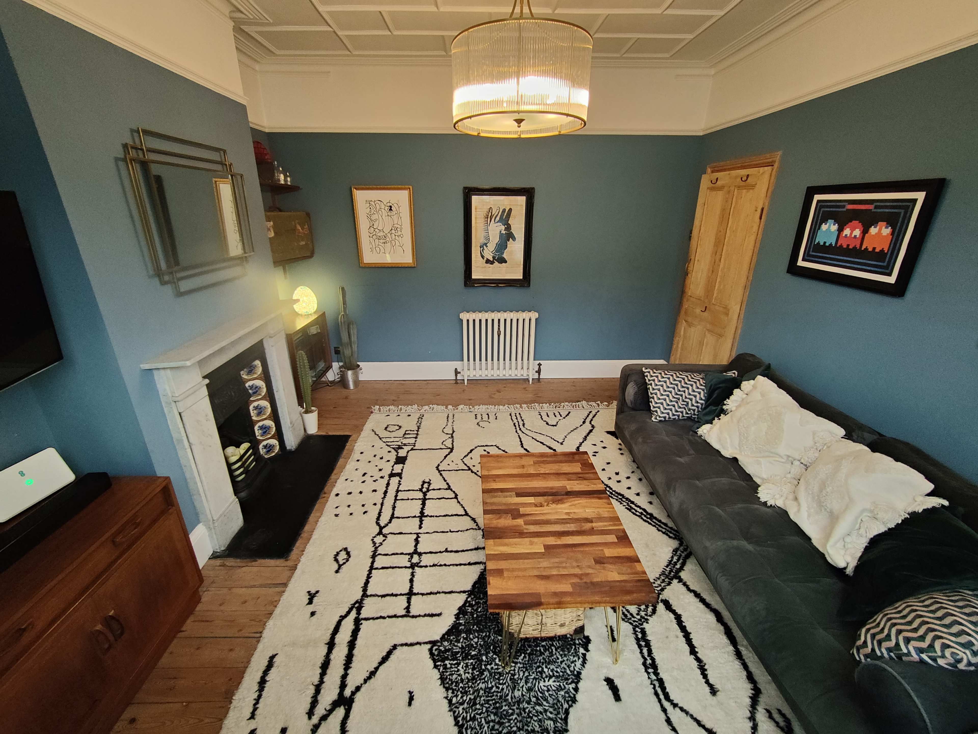 A room with a fireplace, two wall-mounted artworks, a wooden table, and a set of chairs against a blue accent wall.