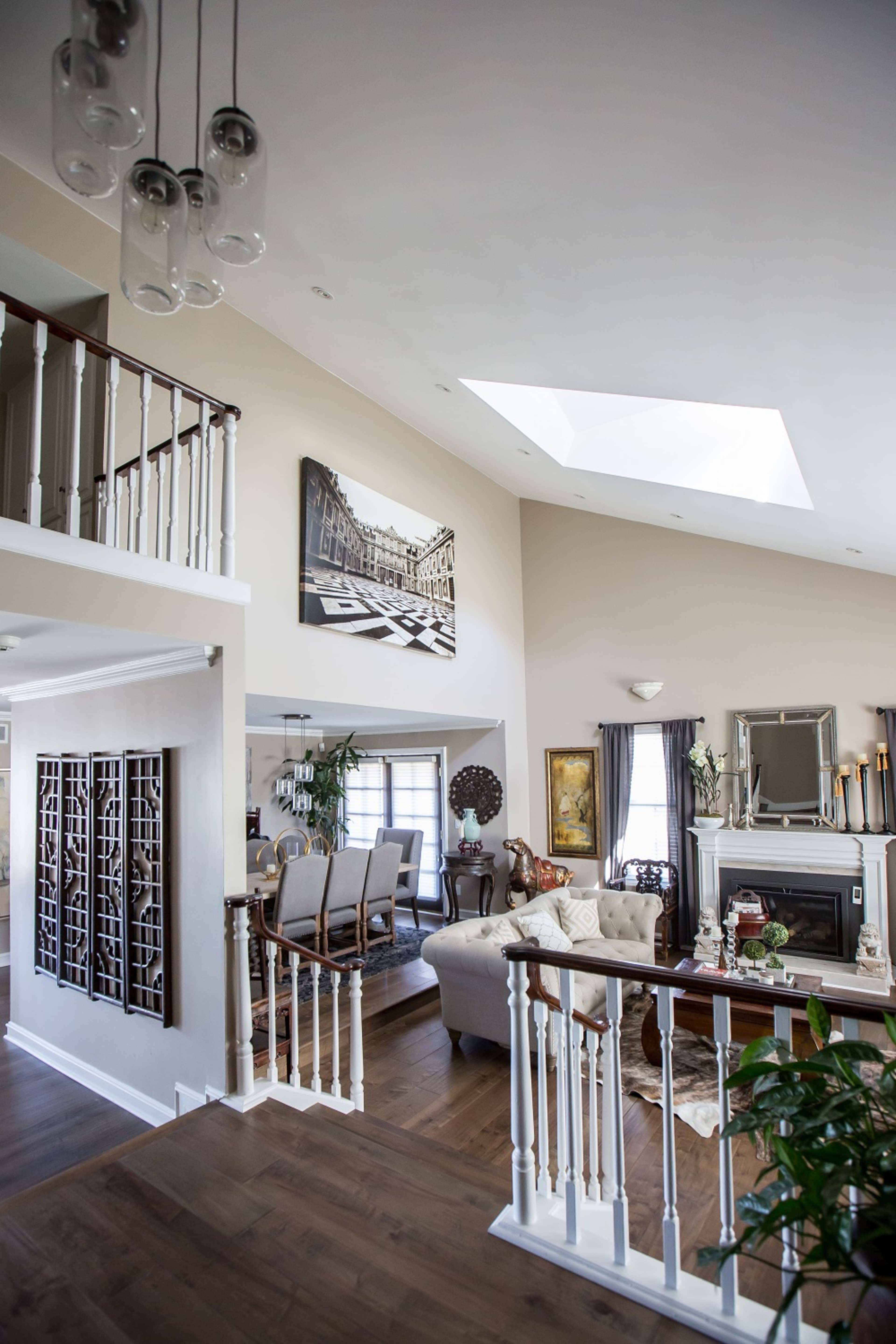 The image shows a spacious, multi-level living area with a skylight, featuring a seating arrangement, dining area, and a decorative fireplace.