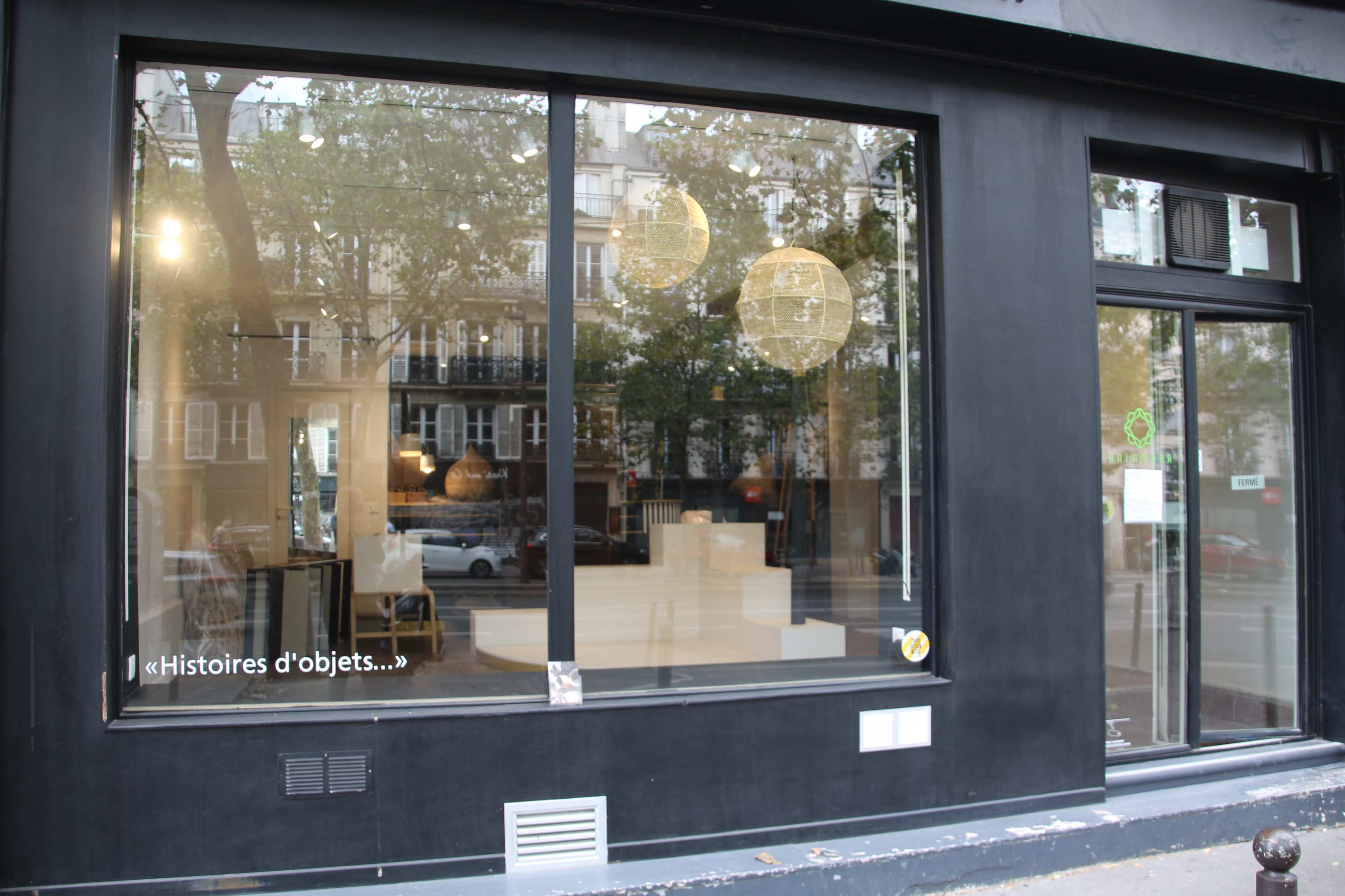 A storefront with large windows displaying minimalist interior decor and two pendant light fixtures.