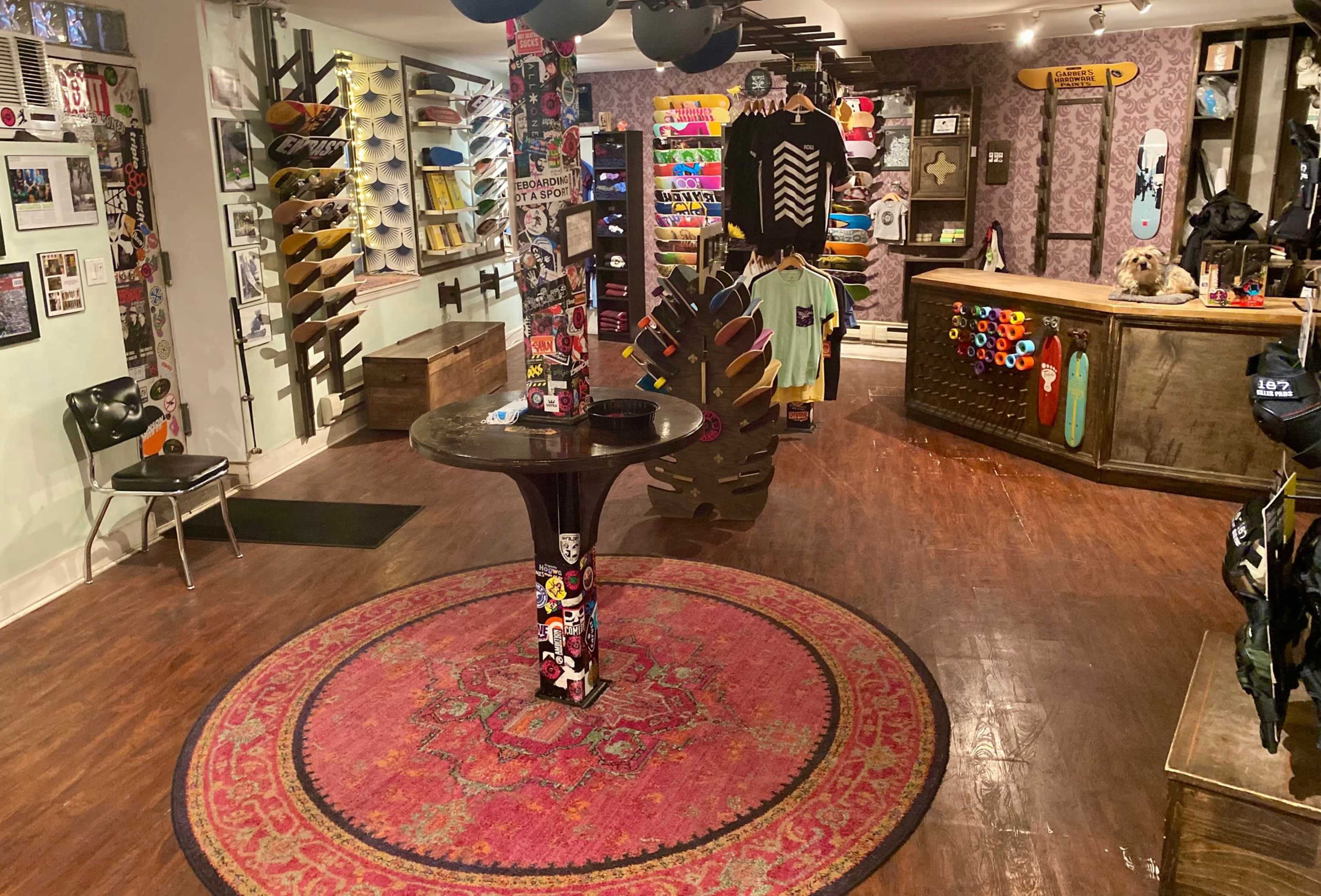An interior of a skateboard shop with various skateboards displayed on walls, a circular rug in the center, and colorful merchandise arranged on a wooden counter.