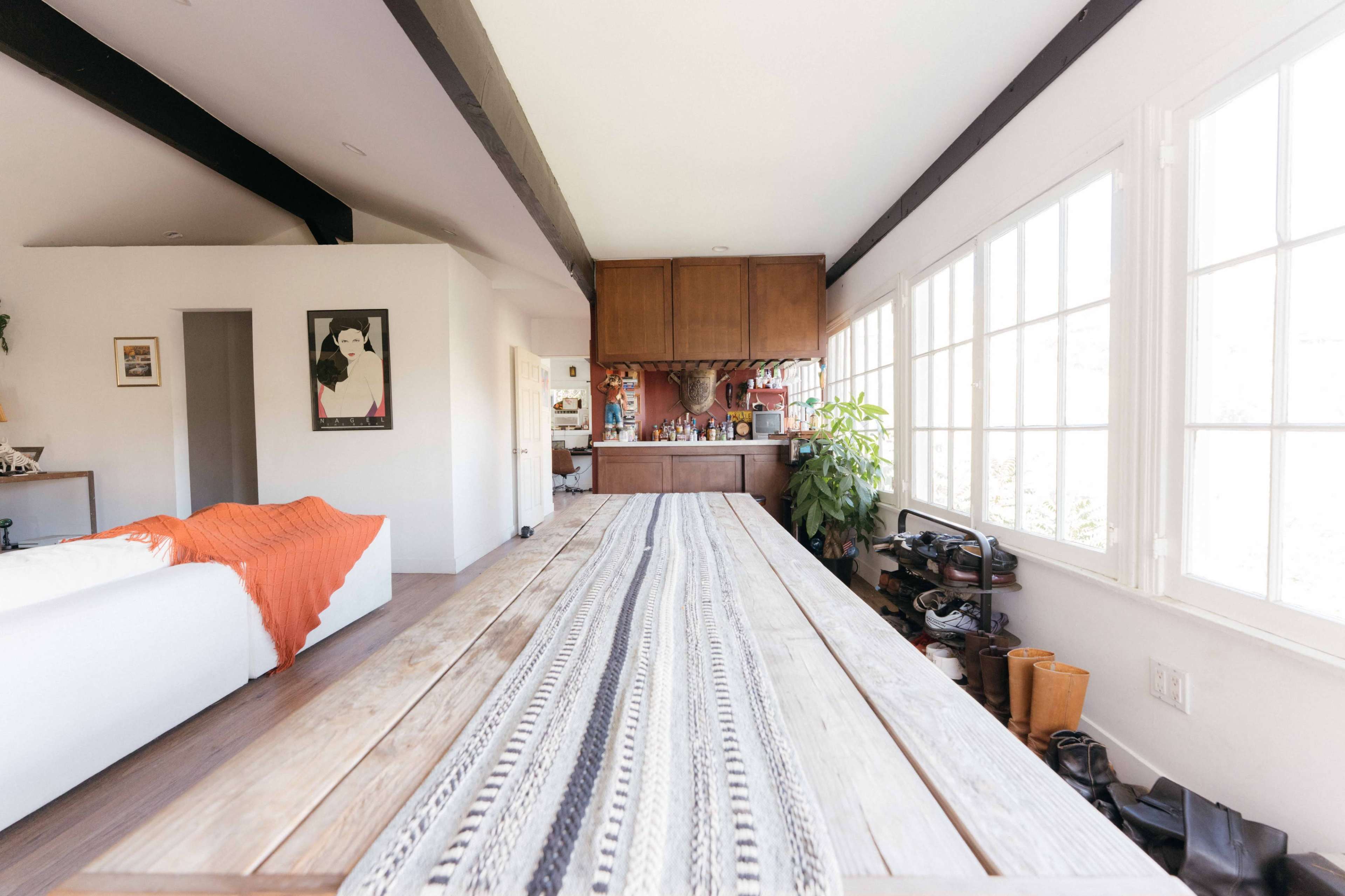 The interior features a long wooden dining table with a patterned runner, surrounded by large windows that allow natural light to fill the space.