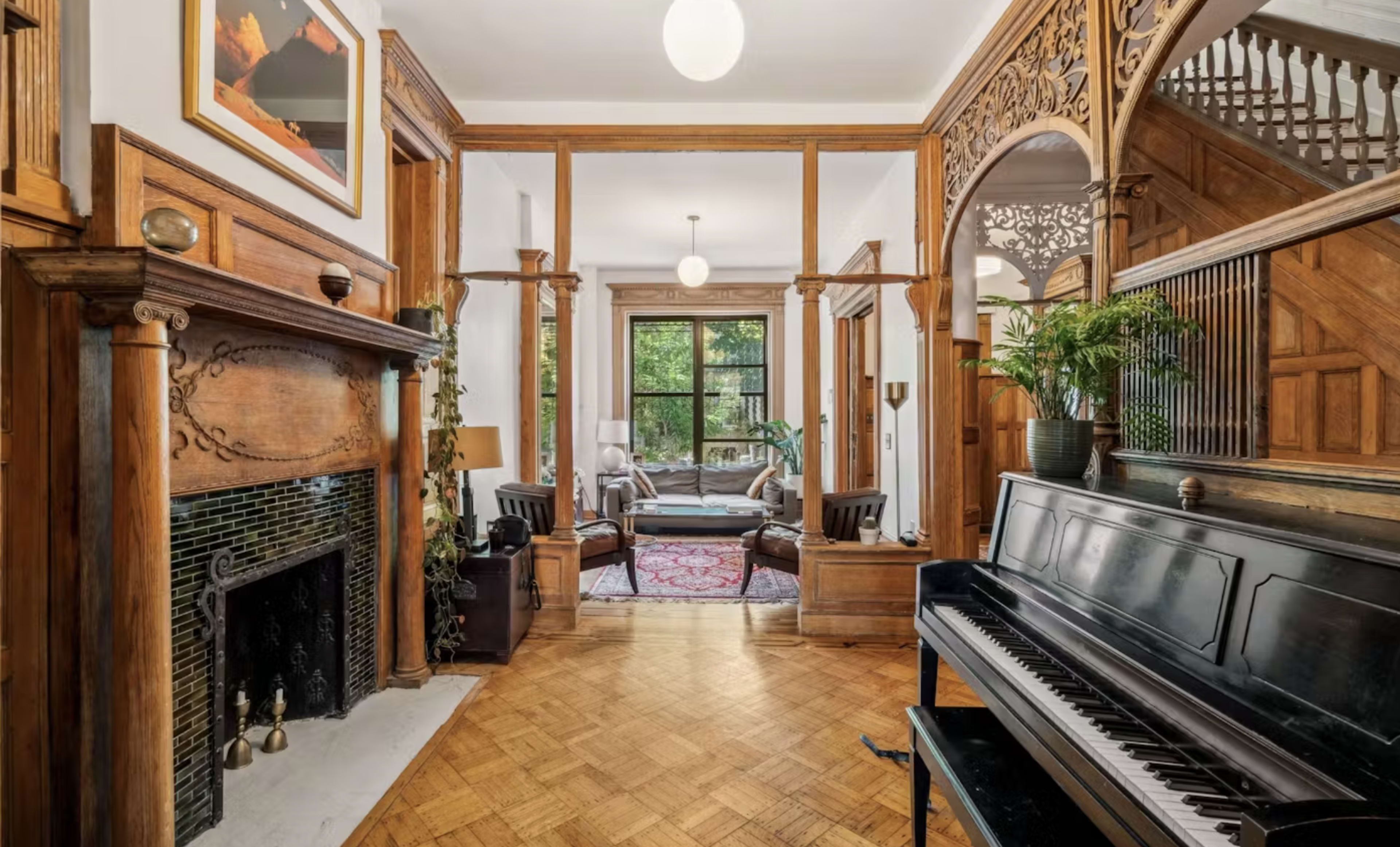 A spacious foyer with a wooden fireplace, a piano in the foreground, and a view of a living area through arched doorways.