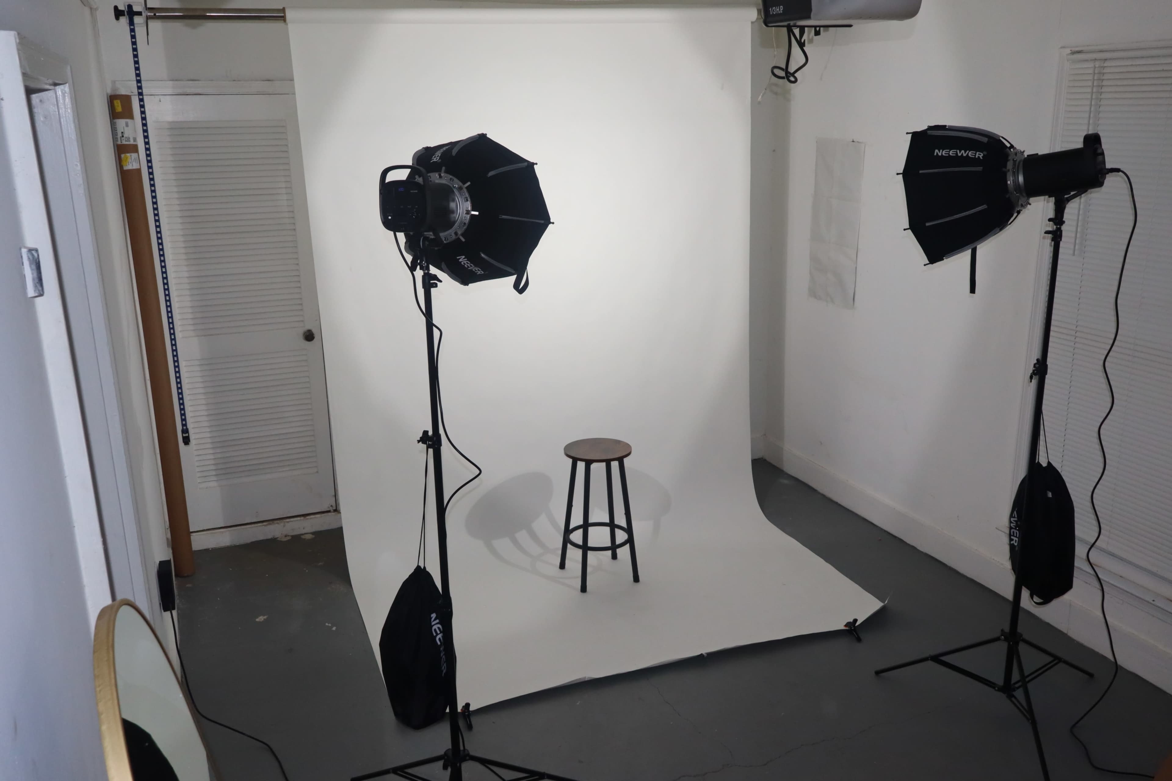 A photography studio setup with two softbox lights facing a wooden stool on a white backdrop.