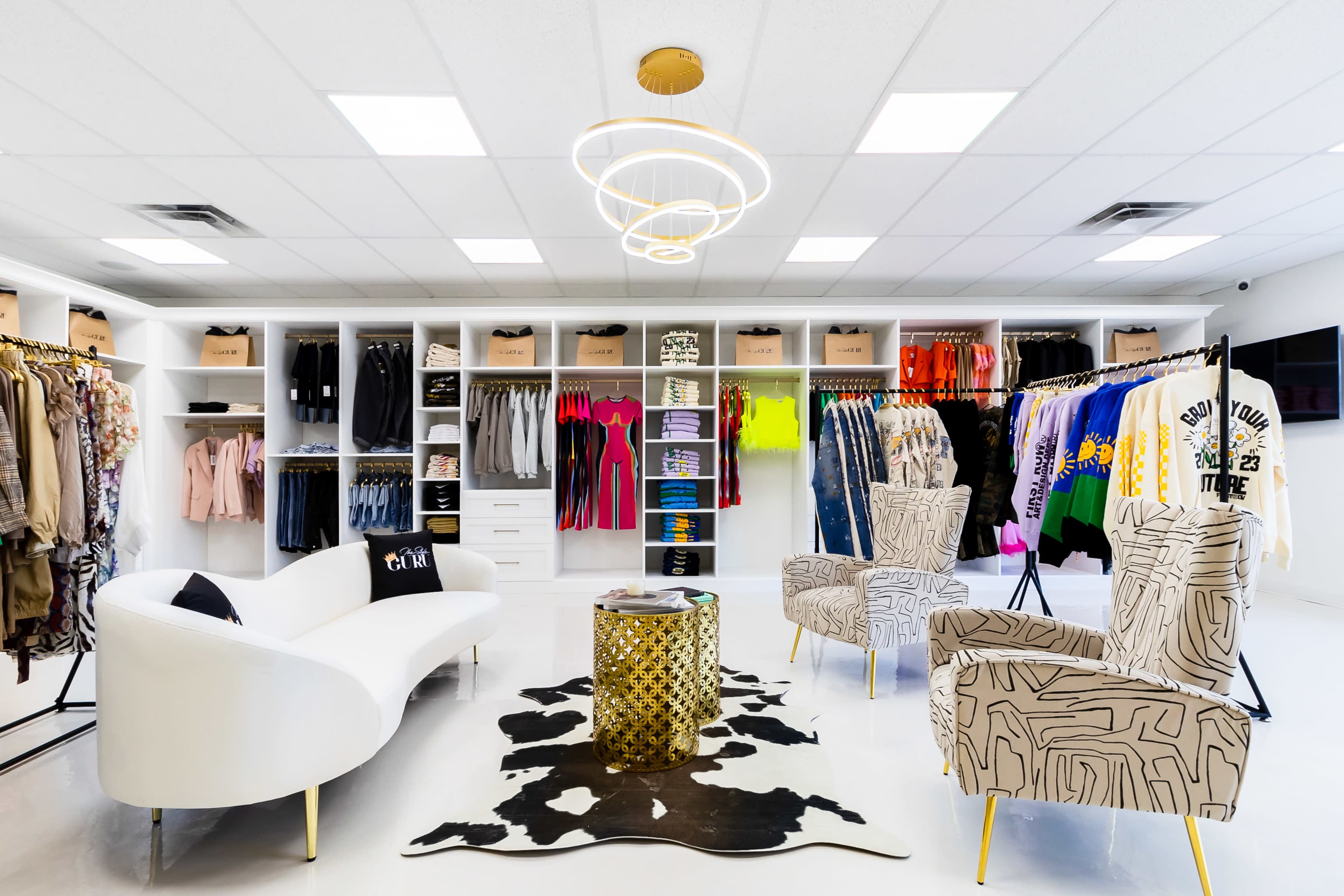 A clothing boutique with neatly organized racks of colorful apparel and stylish seating arrangements in a bright, modern interior.