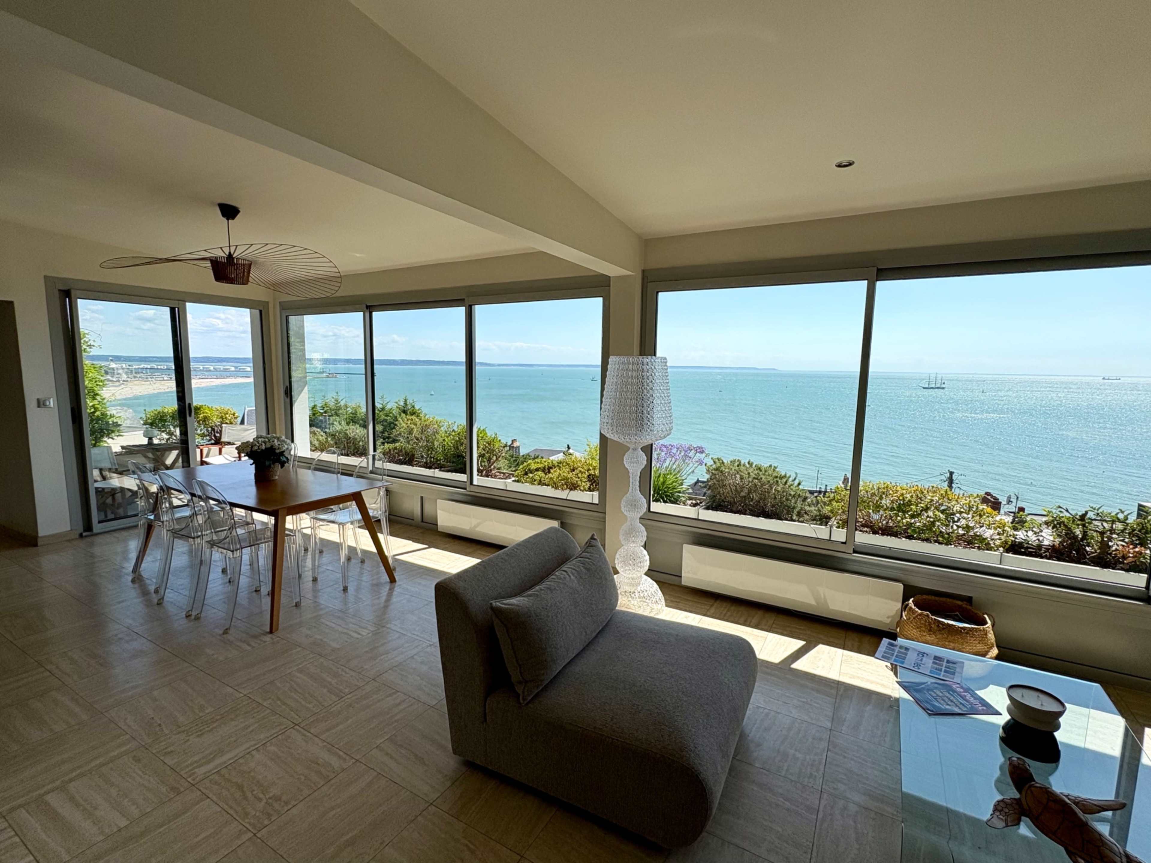 A modern living room with a dining area overlooks a serene coastal view through large windows.