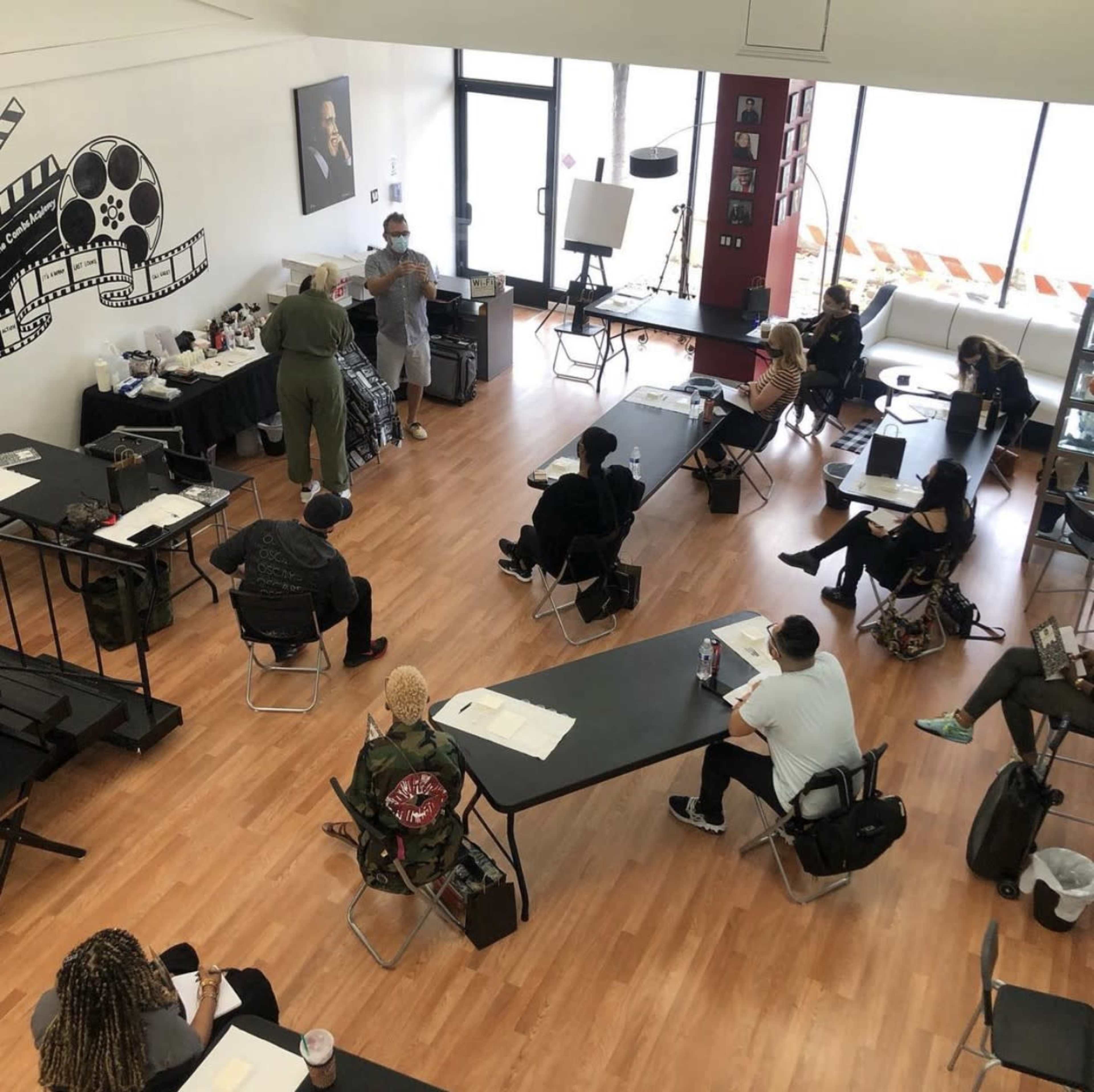 A group of people is seated at desks in a classroom setting, while an instructor addresses them from the front.