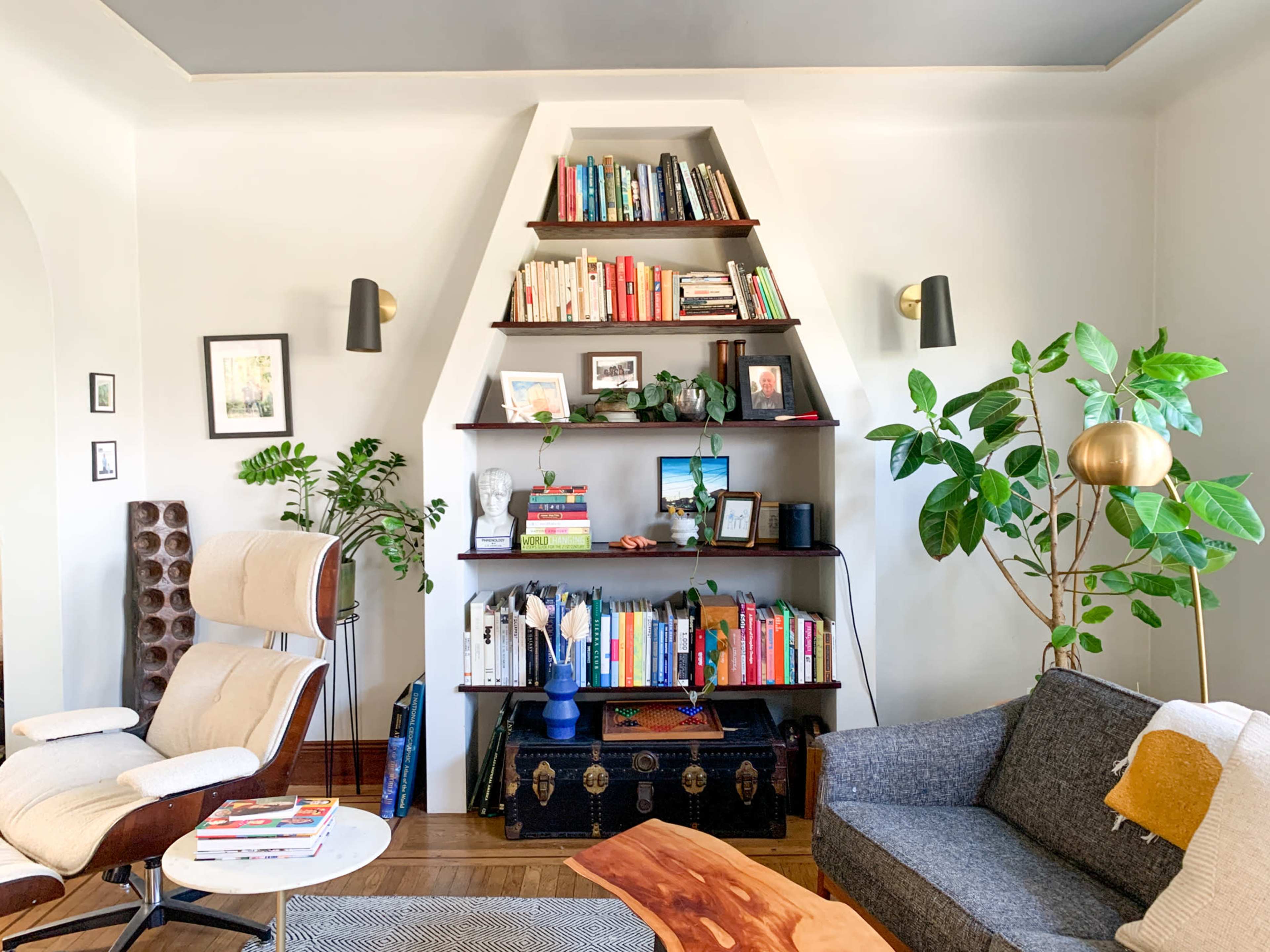 The room features a bookshelf filled with various books, a comfortable chair, a coffee table, and potted plants, creating a cozy living space.