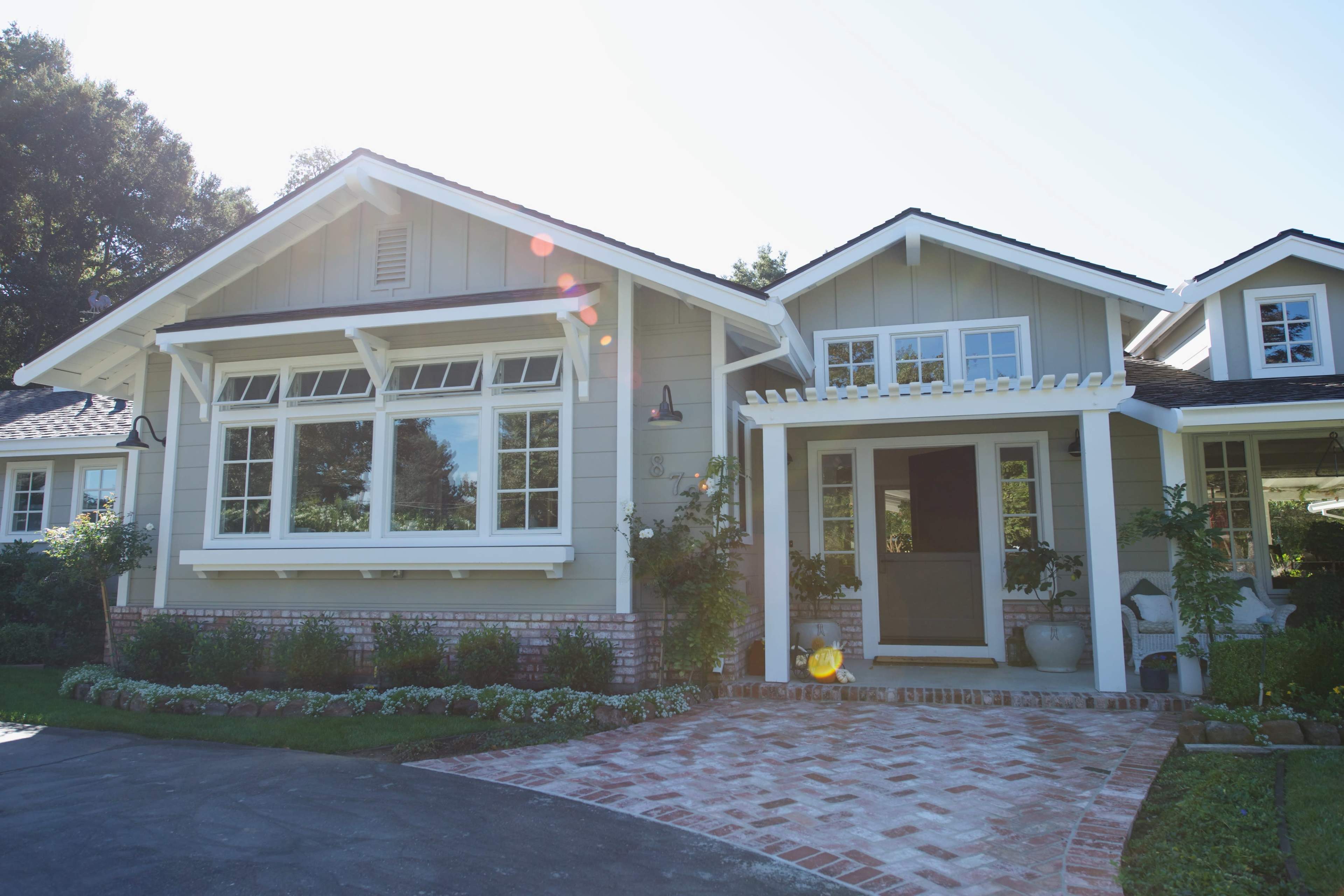 A modern house features a front porch, large windows, and a brick pathway surrounded by greenery.
