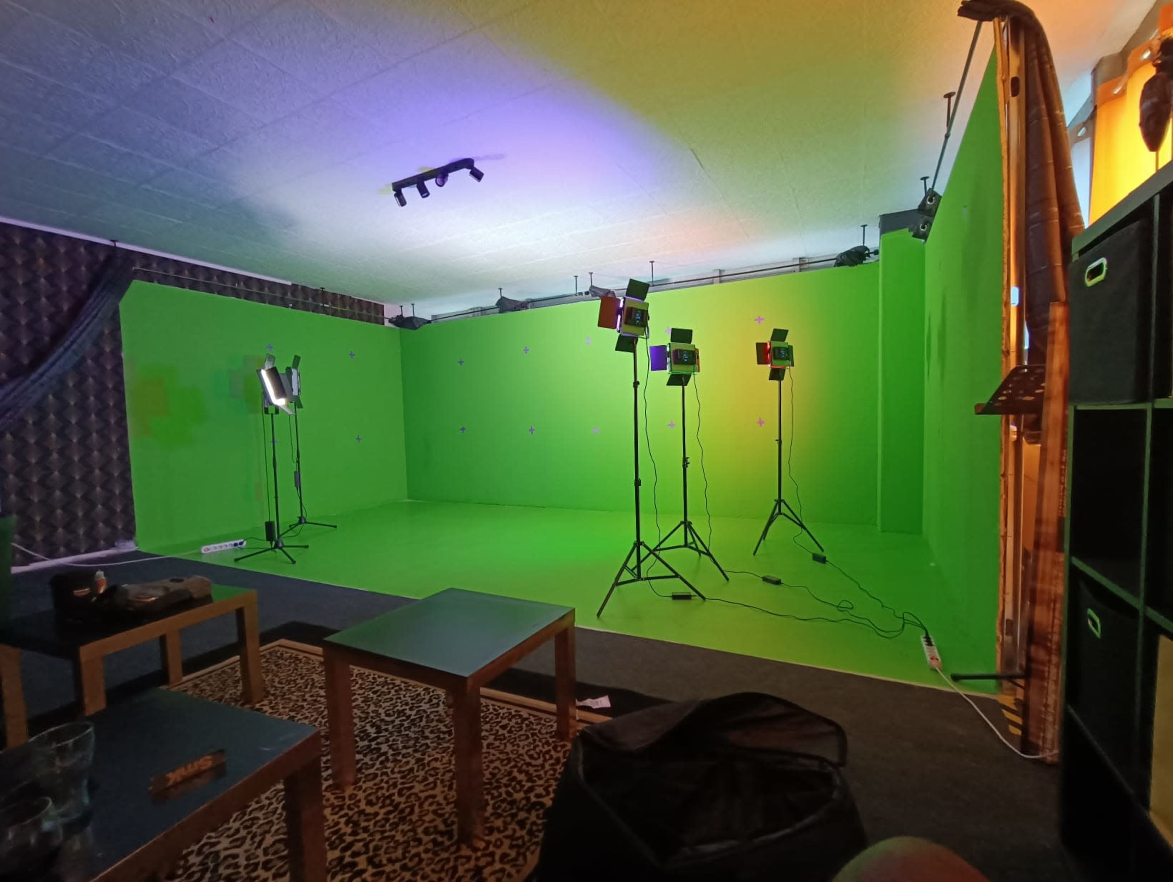 A green screen studio setup with multiple lights, a textured wall, and a few tables in the foreground.