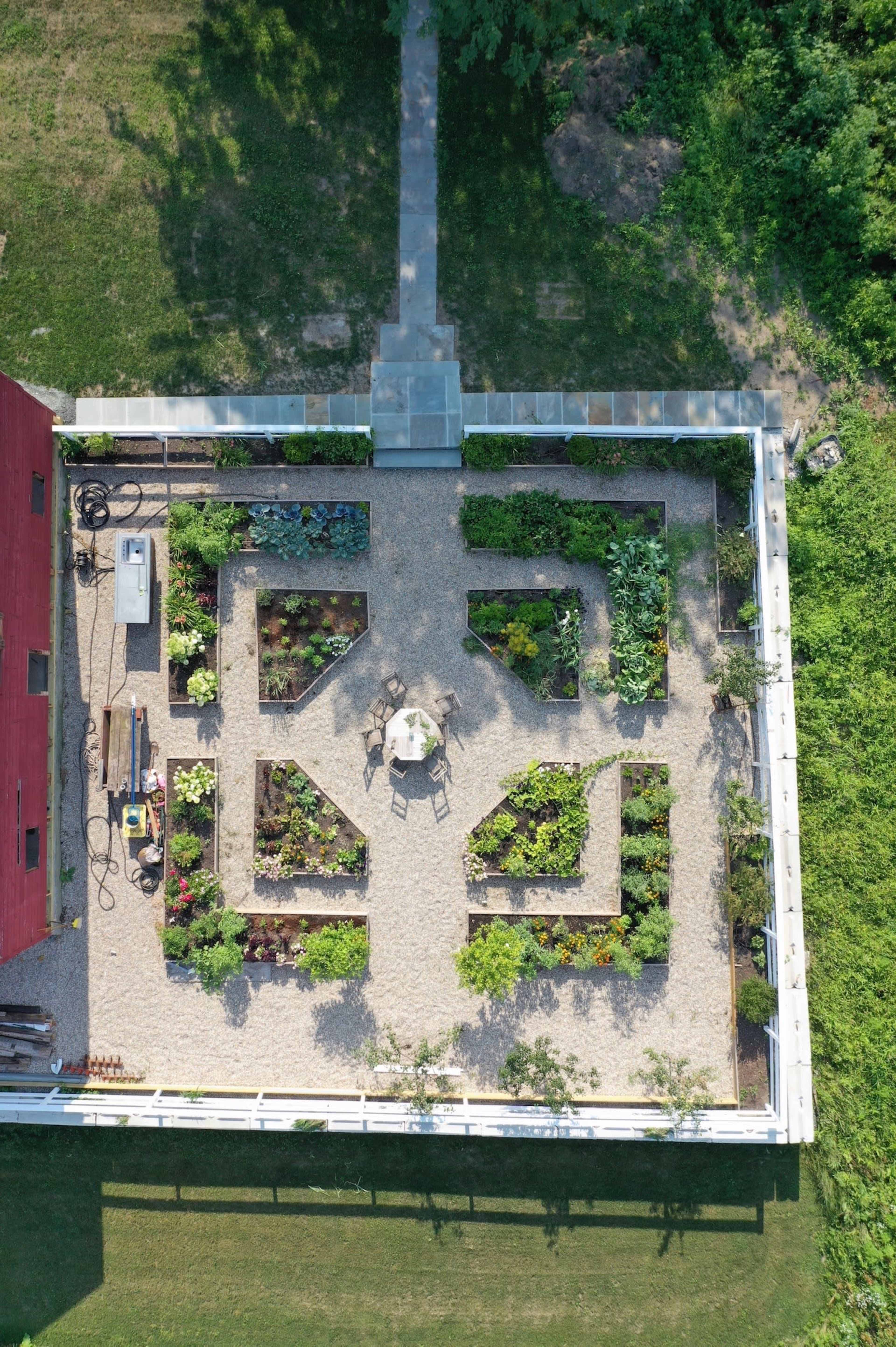 An aerial view of a neatly arranged vegetable garden with raised beds and a central table surrounded by gravel paths.