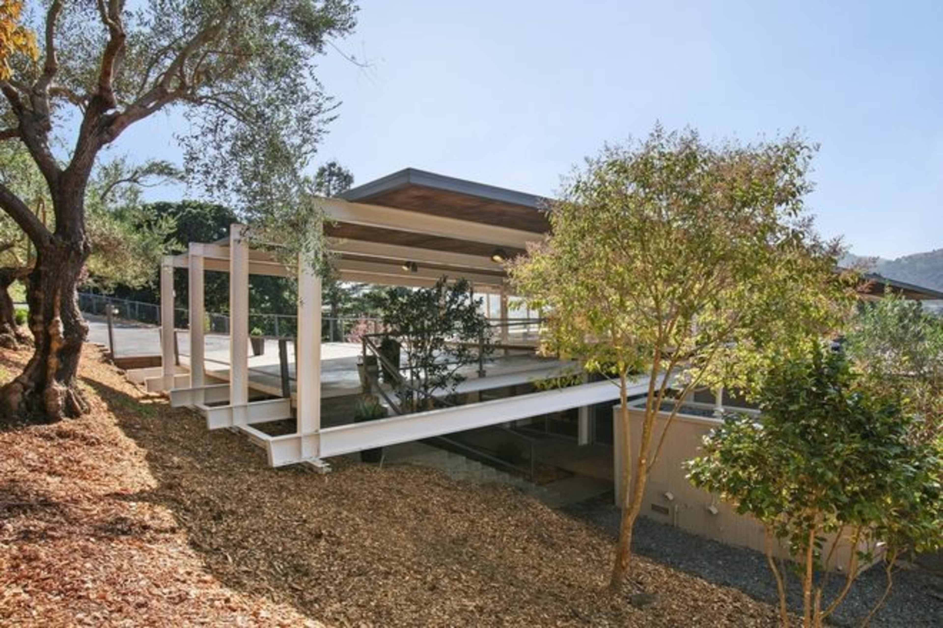 A modern house elevated on a concrete structure surrounded by landscaped grounds with trees and mulch.