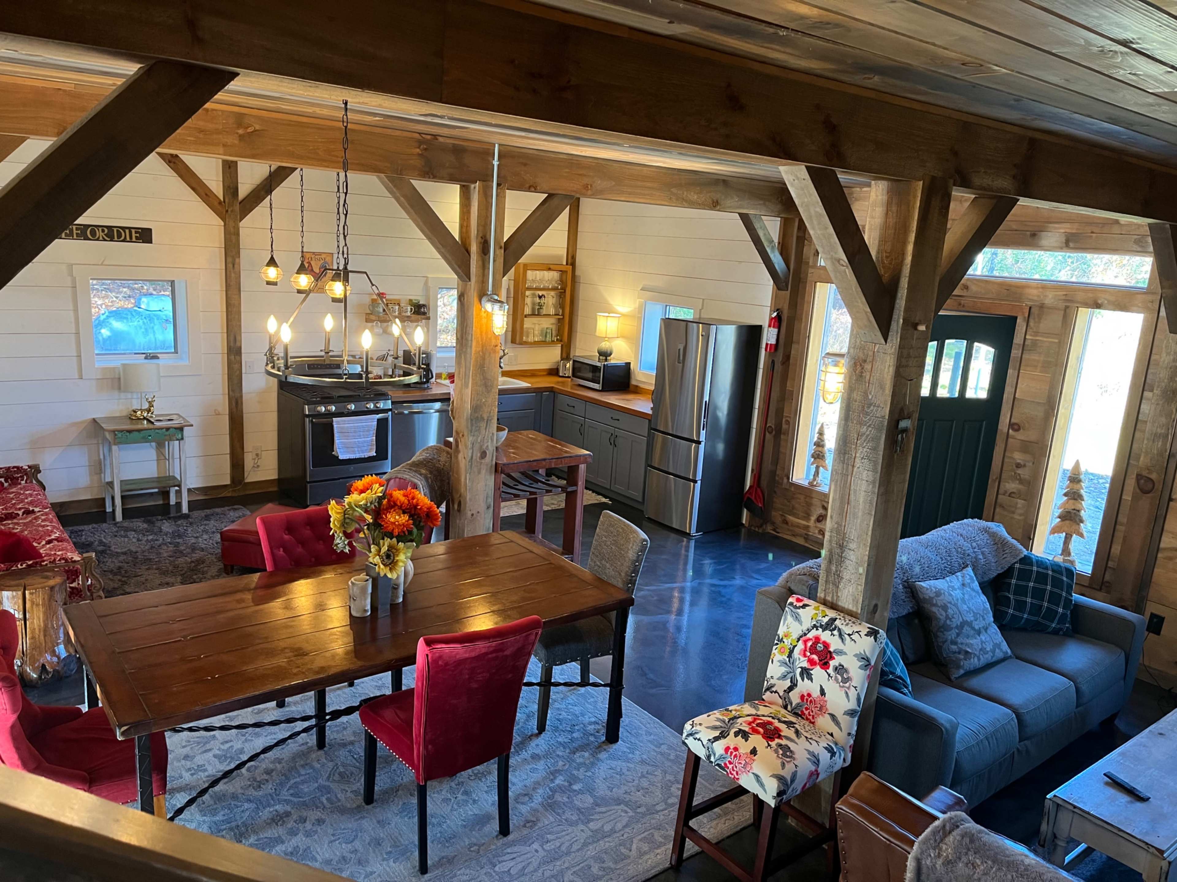A cozy interior of a rustic cabin with a dining area, kitchen, and living room, featuring wooden beams and furniture.