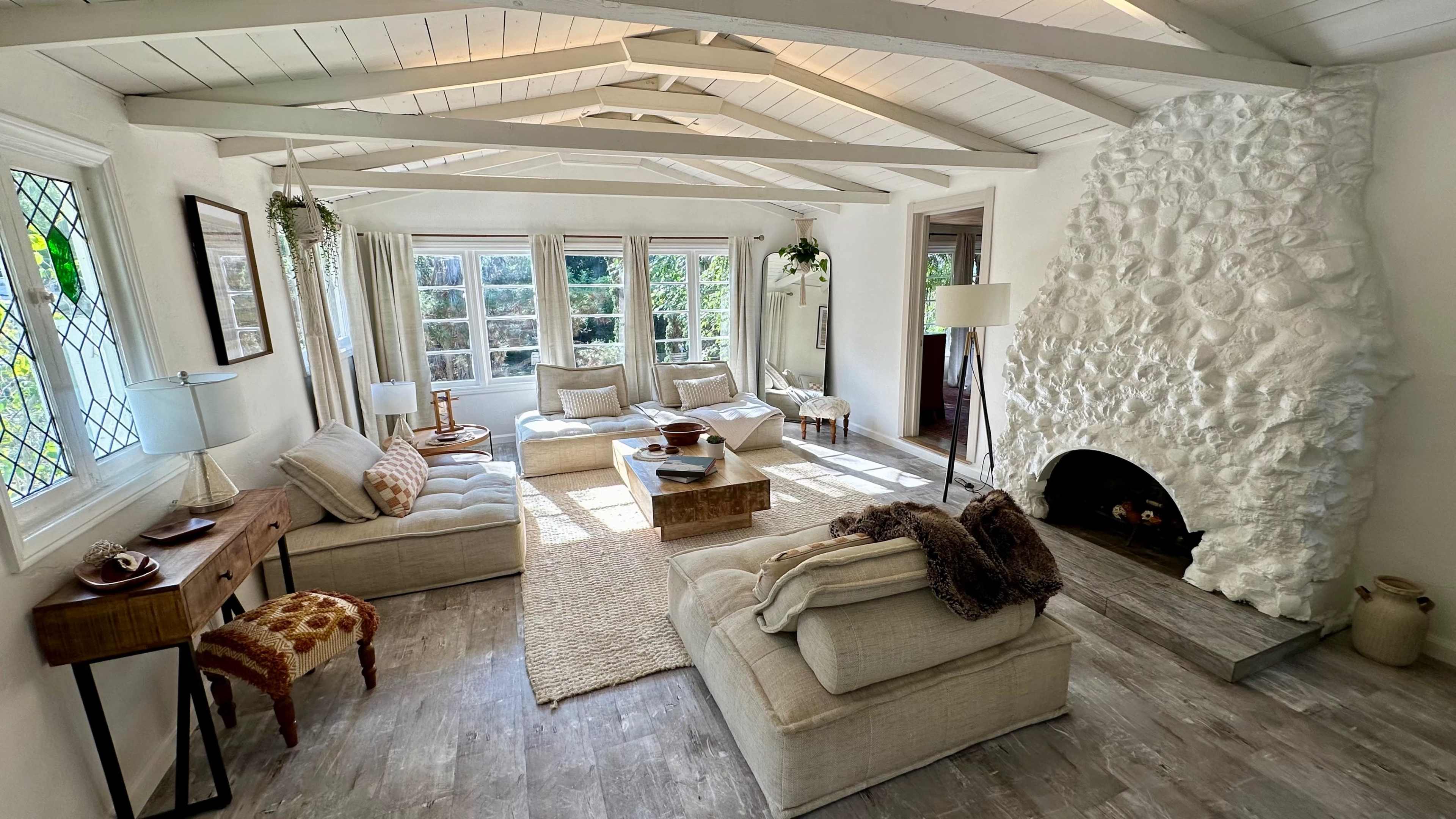 The living room features a cozy arrangement of sofas and a stone fireplace, with large windows allowing natural light to fill the space.