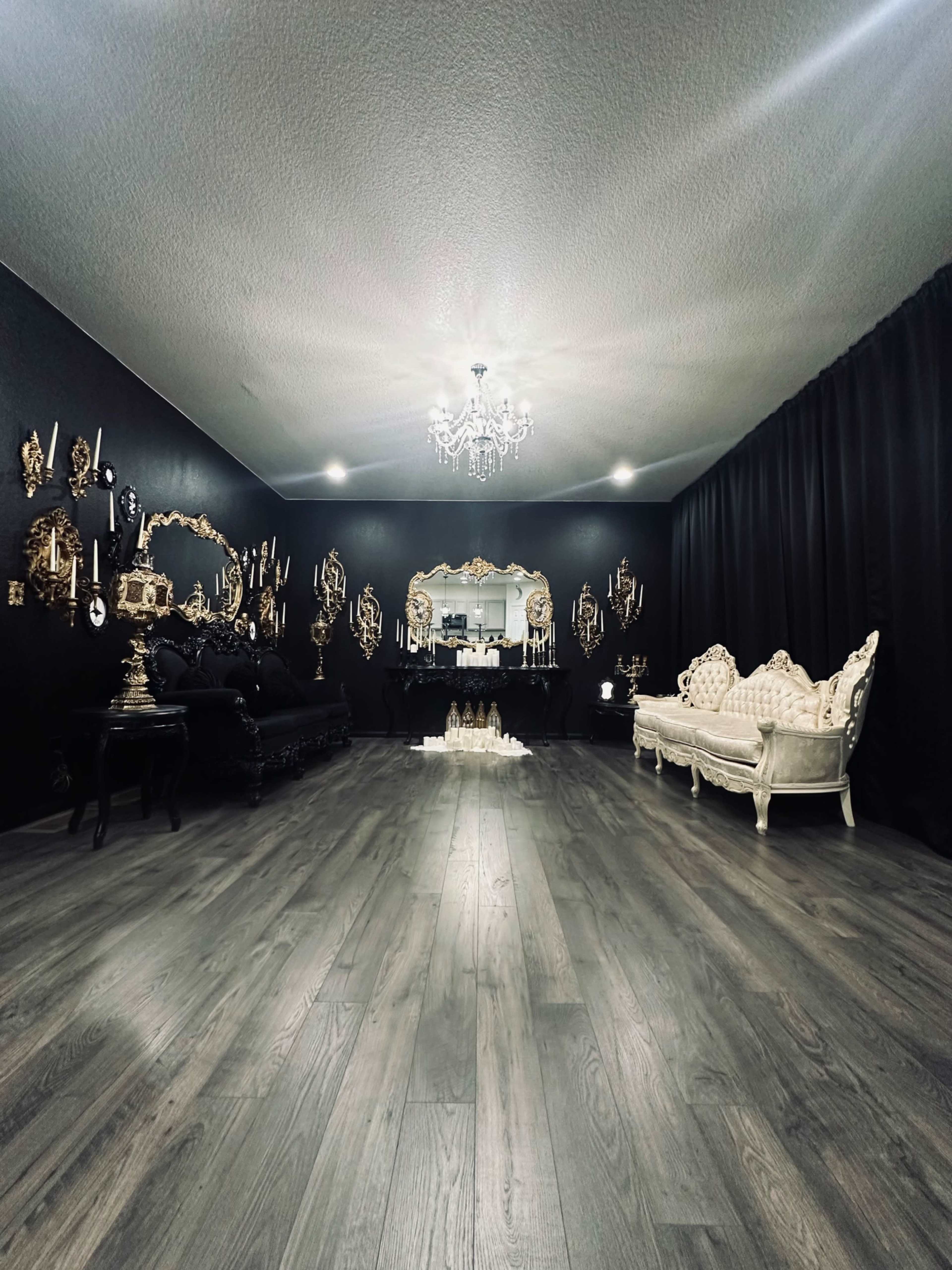 A spacious room with dark walls, a chandelier above, and ornate furniture arranged around a central decorative display.