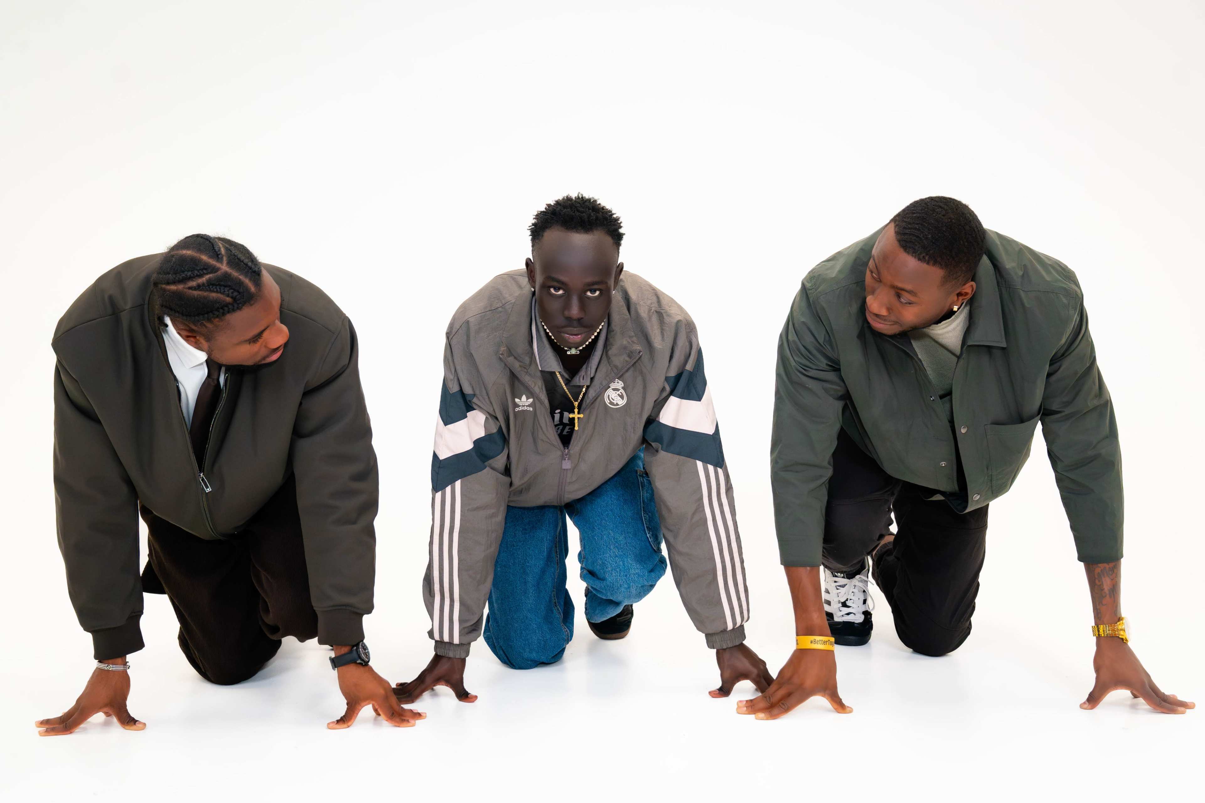 Three men are positioned on their hands and knees, facing the camera, on a white background.