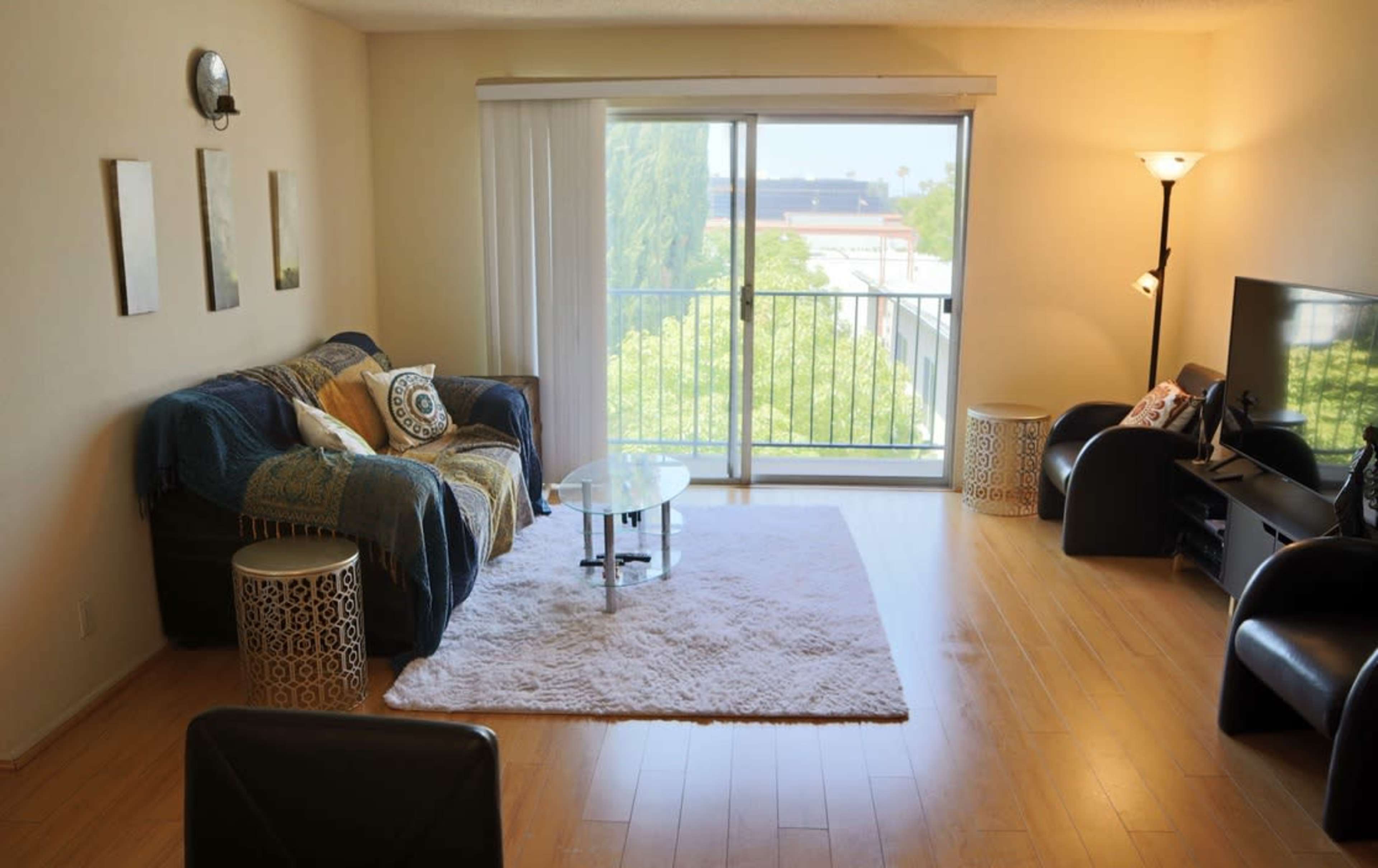A bright living room features a couch, a glass coffee table, and a large window overlooking greenery.