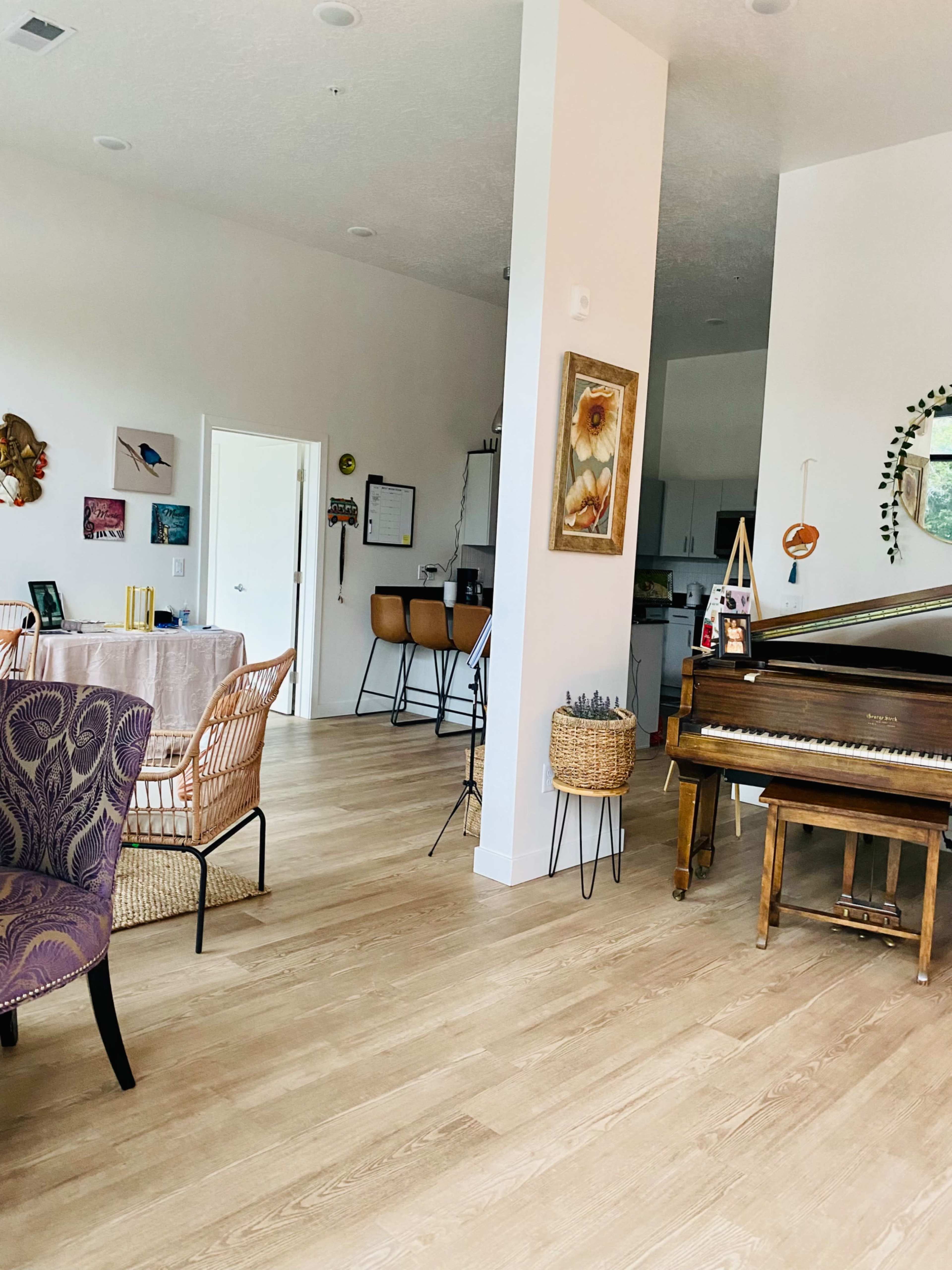 A spacious, open interior featuring a dining area with a table, a piano, and a kitchen visible in the background.