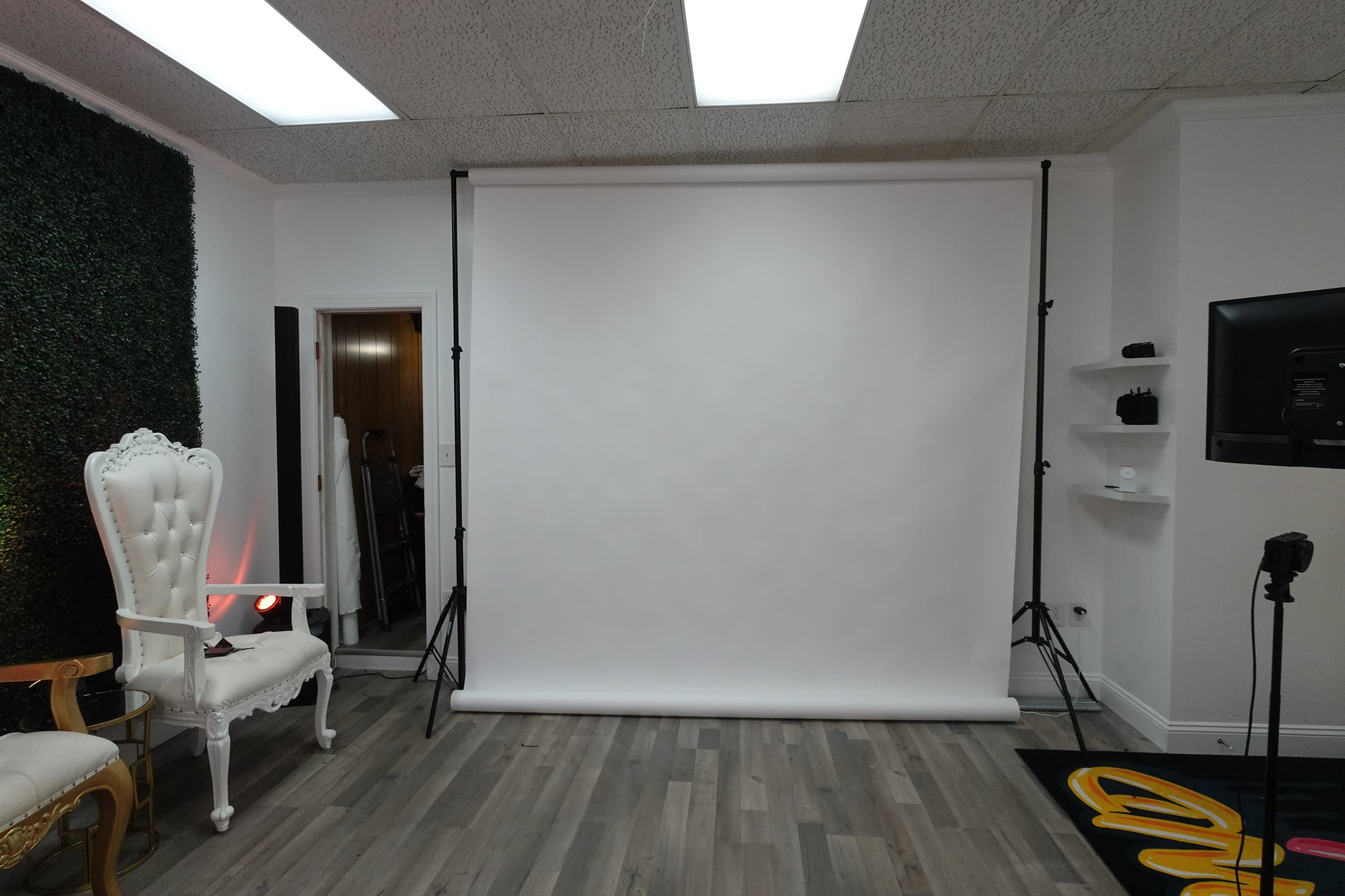 A studio setup with a plain white backdrop, adjustable stands, and a decorative chair on the side.