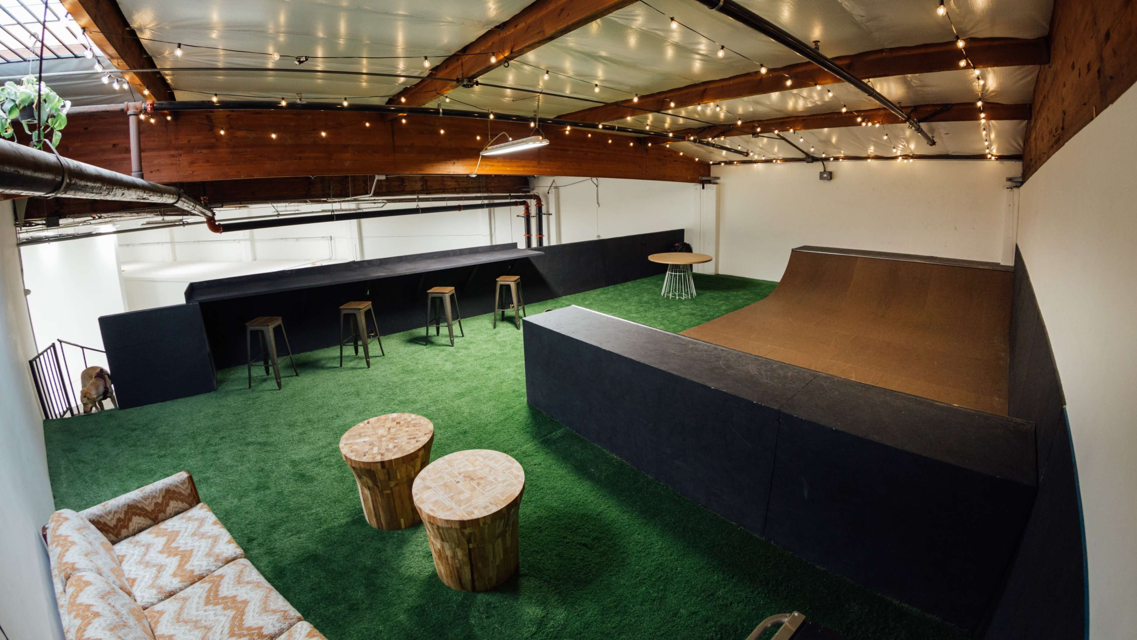 The interior space features a mini skate ramp, seating areas, and decorative string lights against a backdrop of green artificial turf.