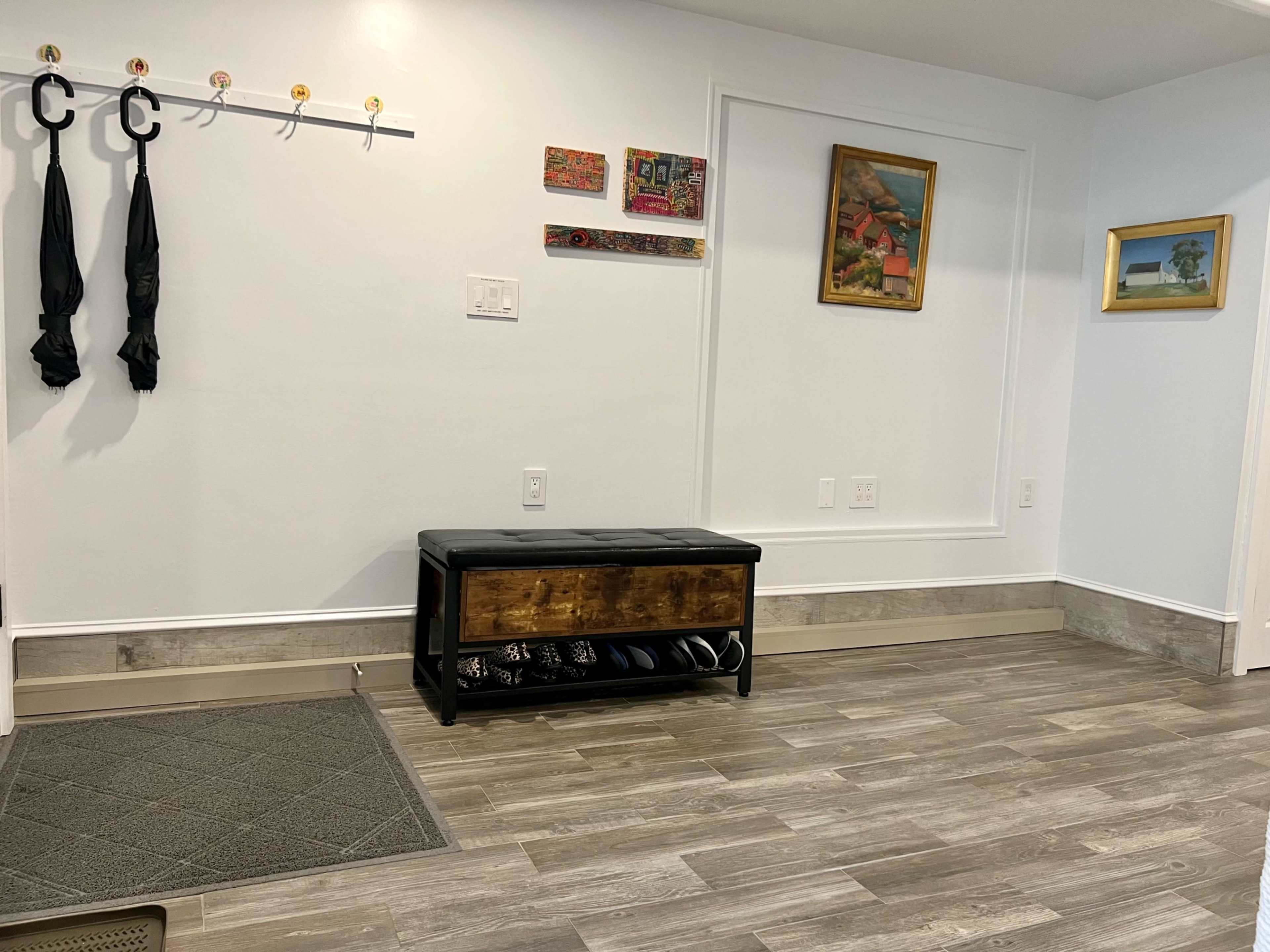 The image shows a hallway with a coat rack, a decorative wall gallery, and a storage bench with shoes underneath it.