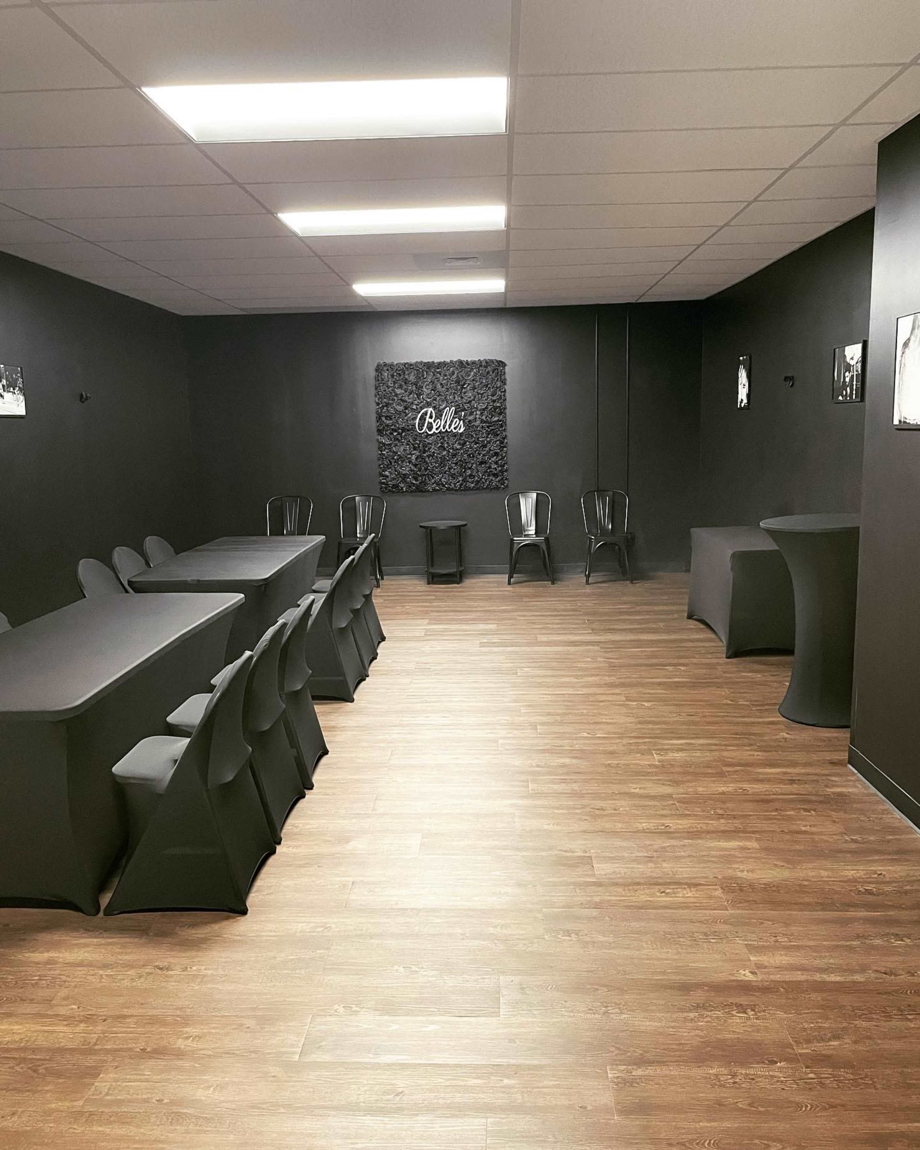 A modern, minimalist room with black walls and furniture, featuring a long table with chairs and a small bar-type table in the corner.