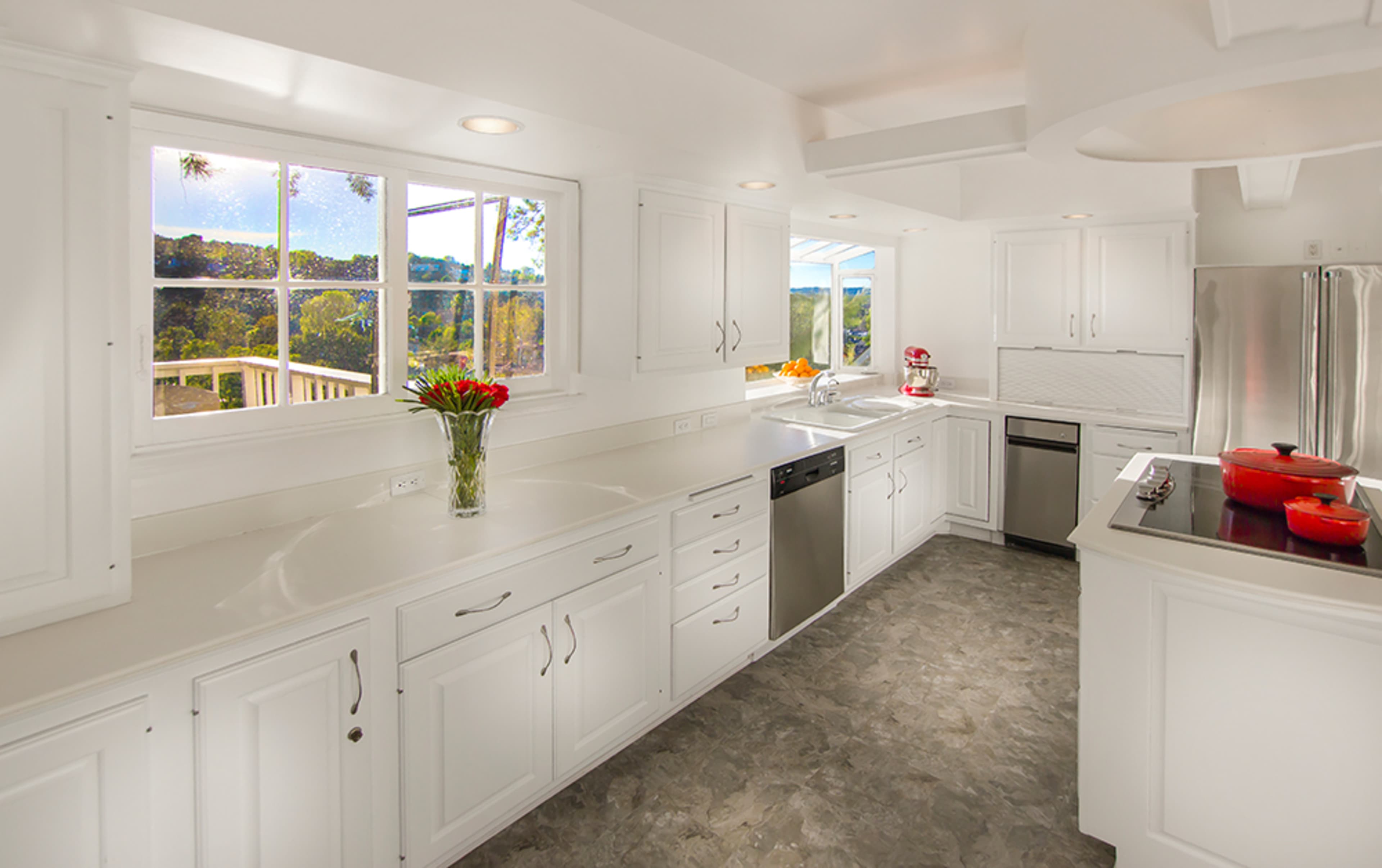 A bright and modern kitchen features white cabinetry, stainless steel appliances, and a large window with a scenic view.