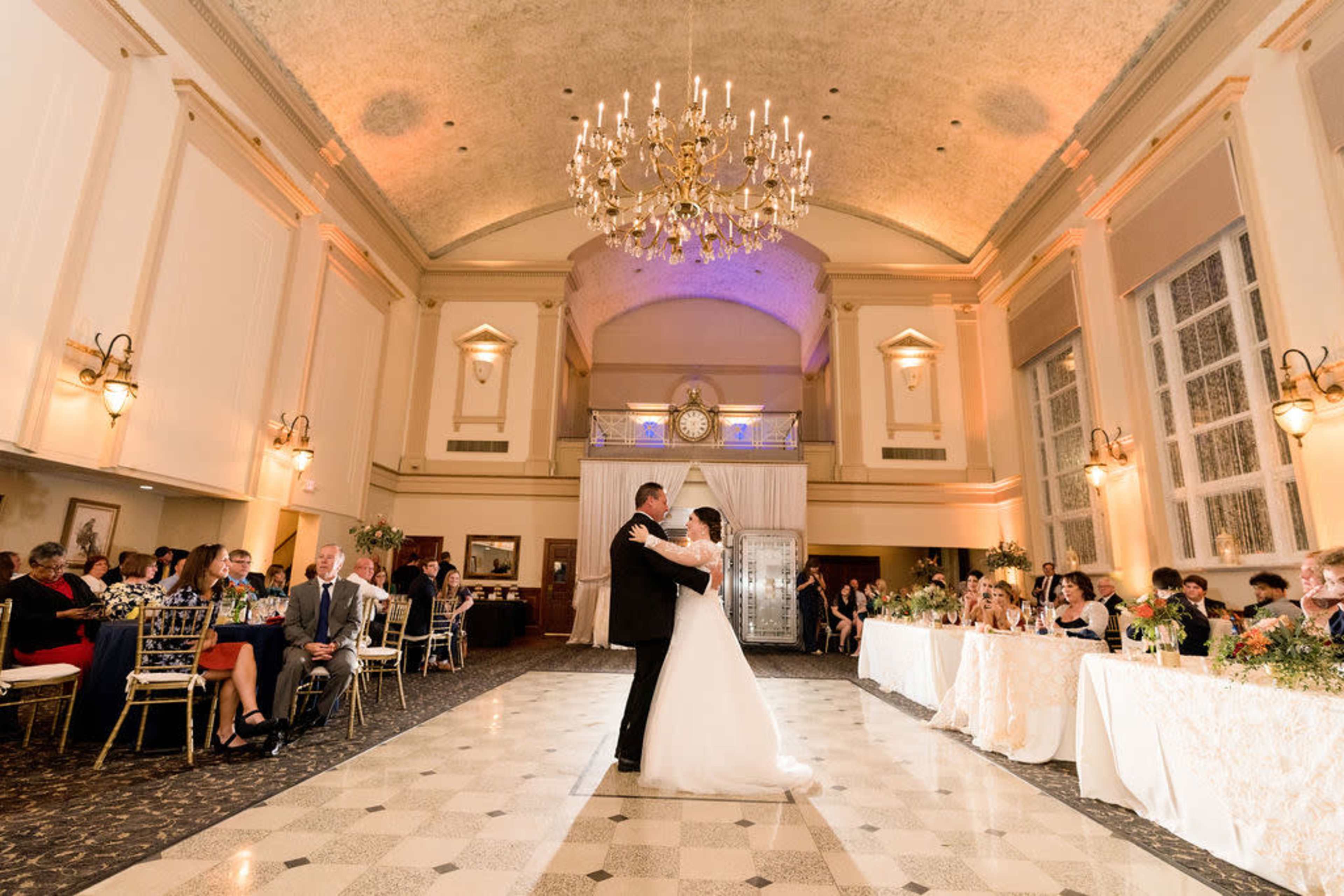 A bride and groom share their first dance in a grand hall decorated for a wedding reception.