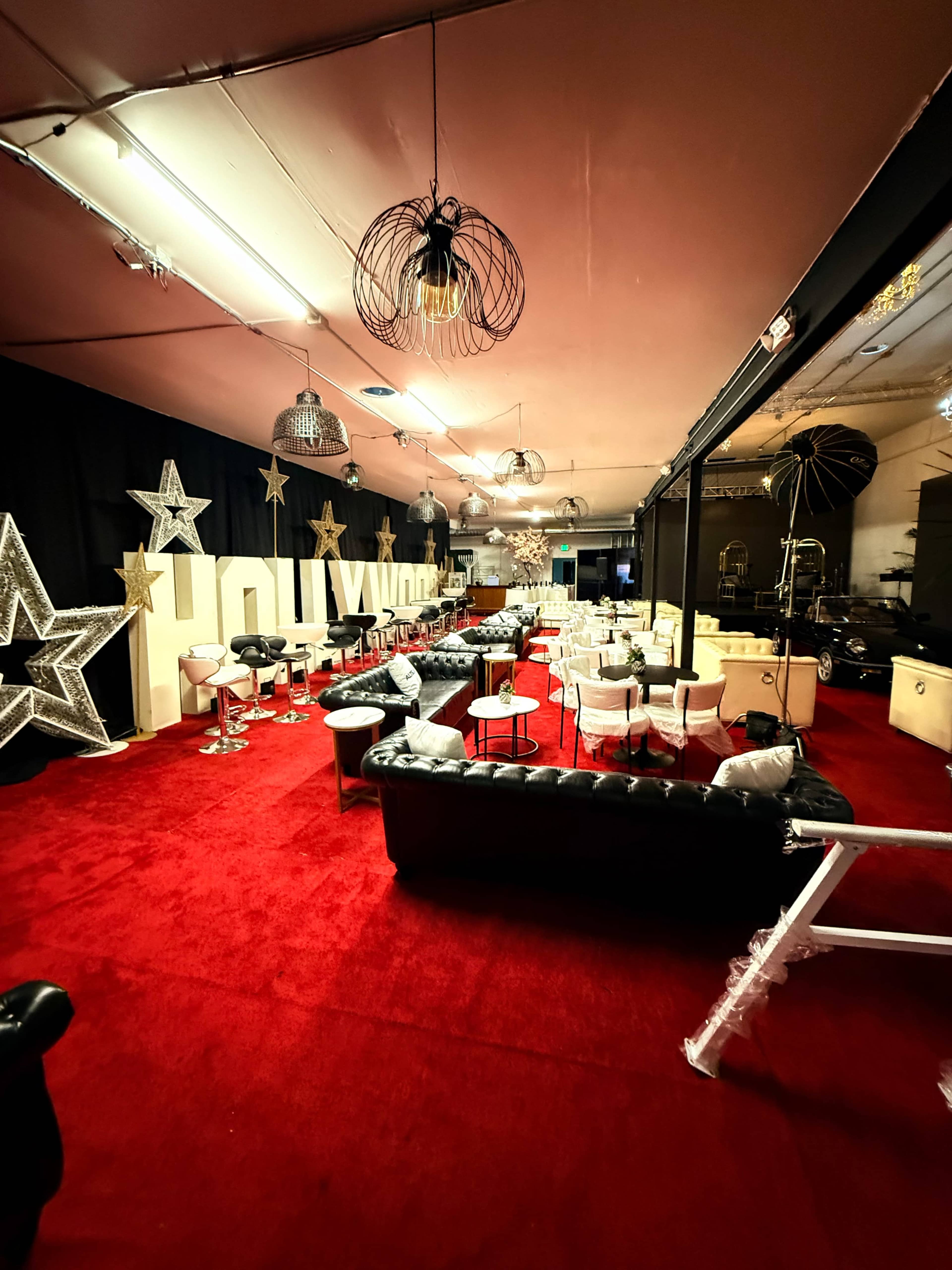 The image depicts a spacious event area decorated with large gold stars, plush seating, and a red carpet, creating a glamorous atmosphere.