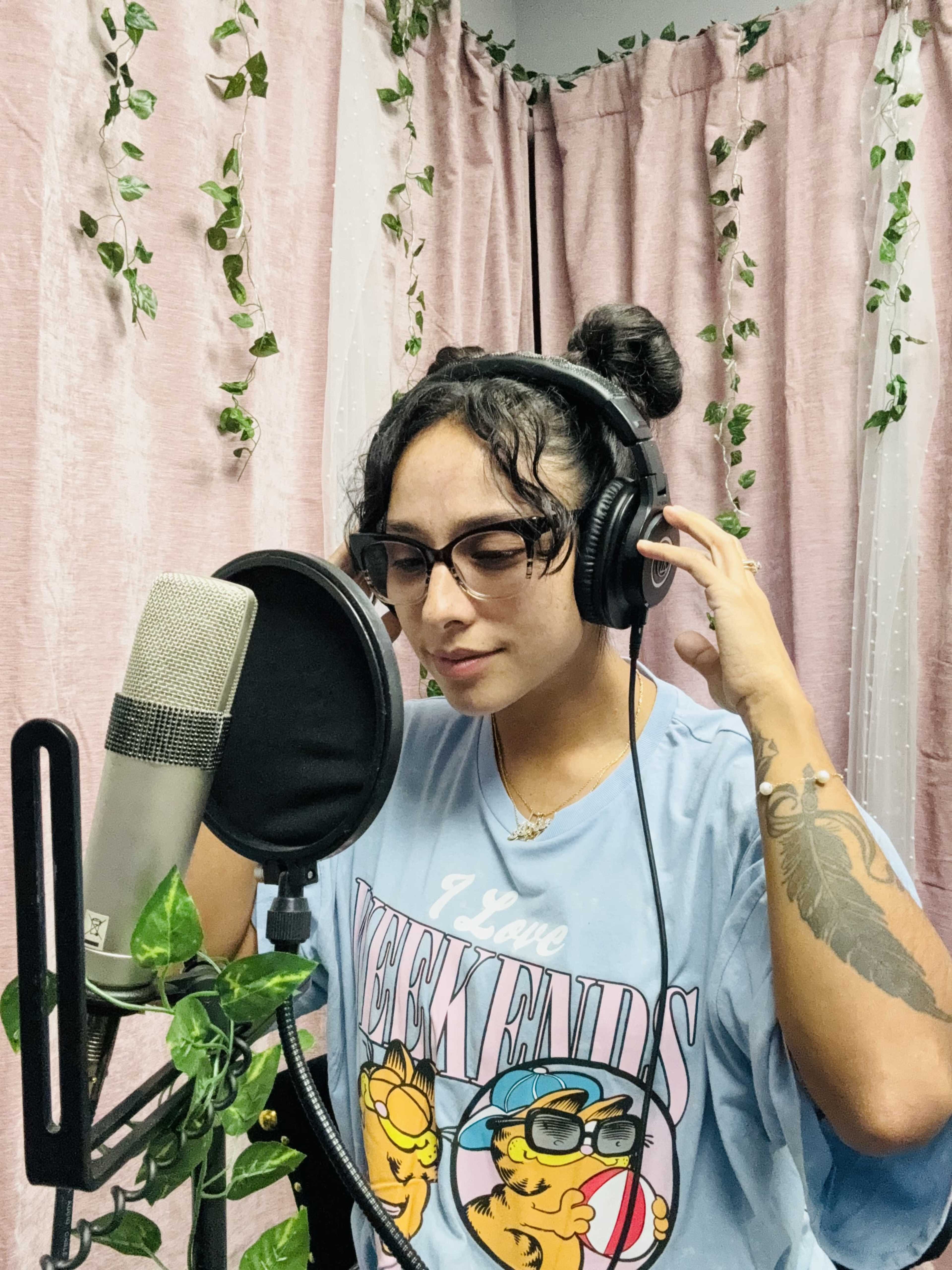 A person wearing headphones is recording vocals in a studio surrounded by pink curtains and hanging greenery.