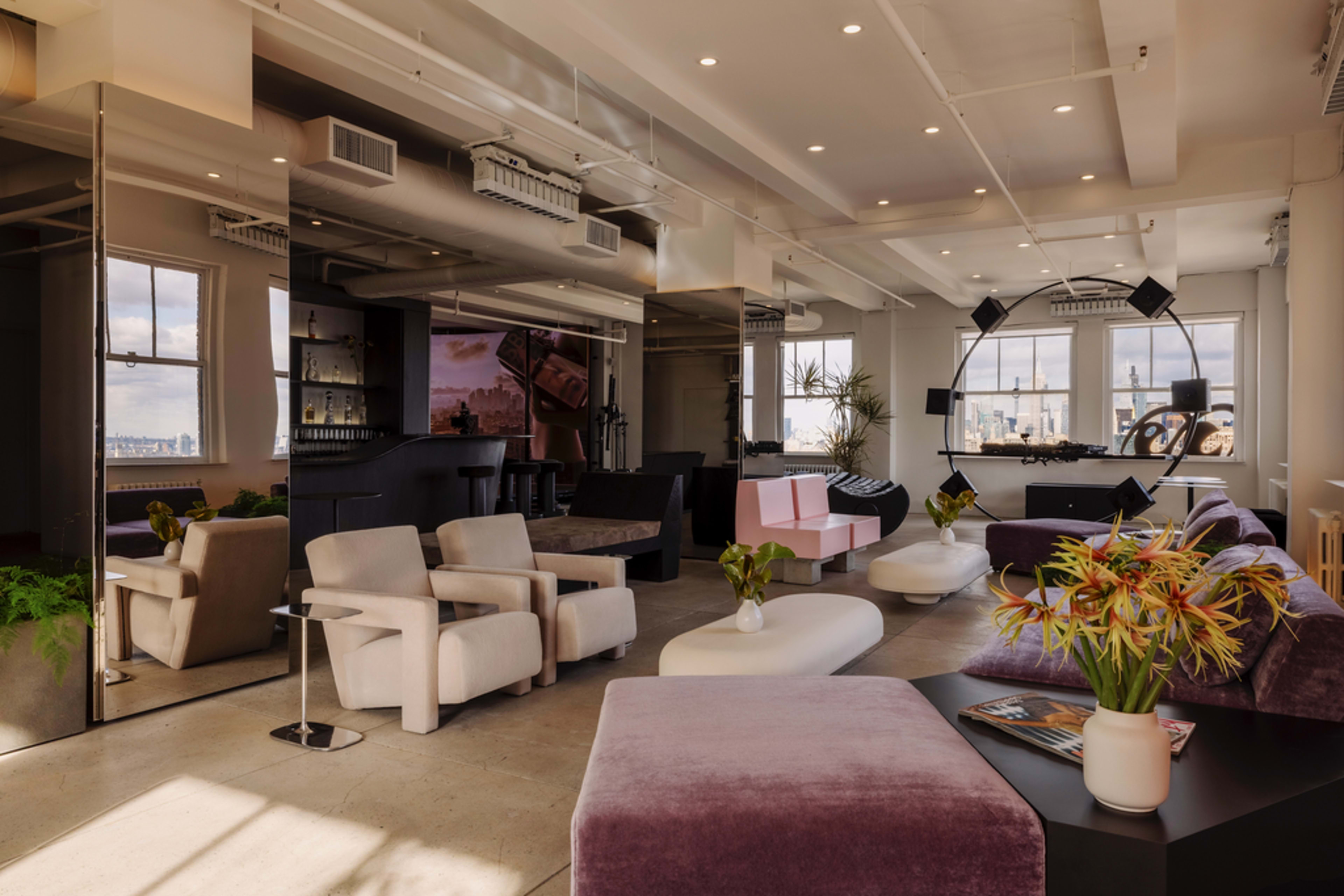 The image shows a modern, spacious lounge area with various seating options, large windows, and a sleek bar setup.