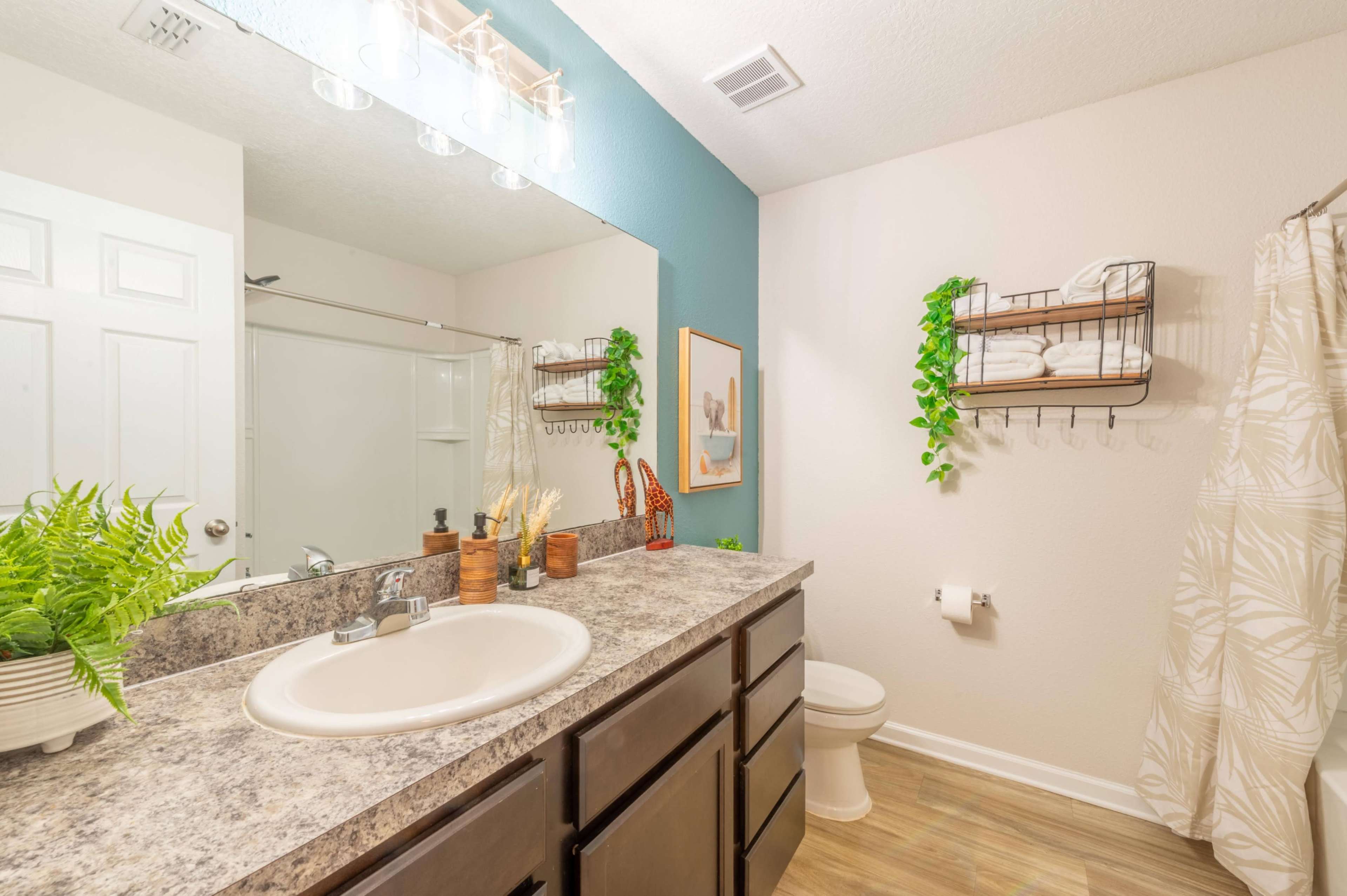 A bathroom with a sink, mirror, and shower area, featuring plants and neatly arranged towels on display.