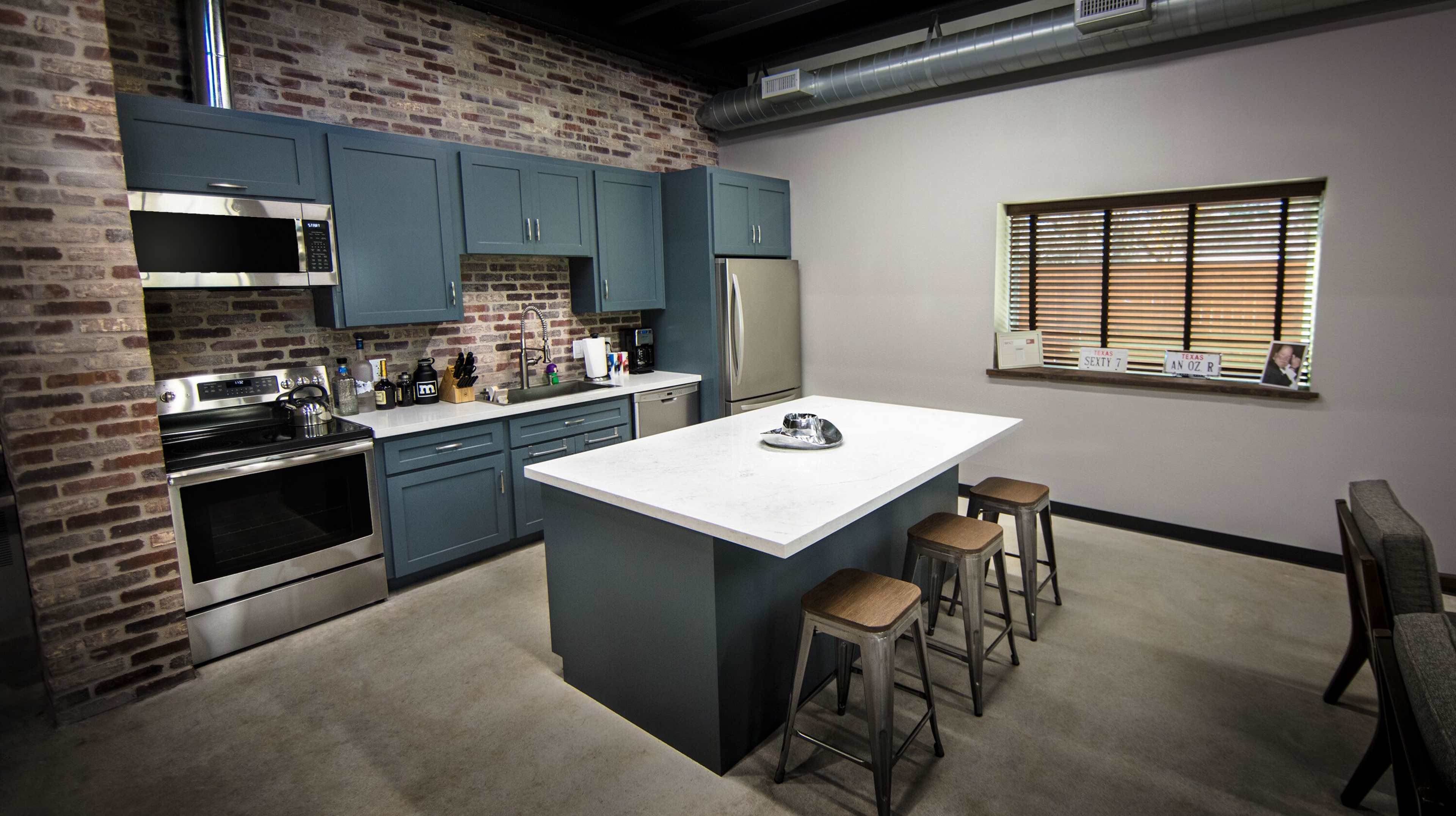 A modern kitchen featuring blue cabinetry, stainless steel appliances, and a white marble island with three wooden stools.