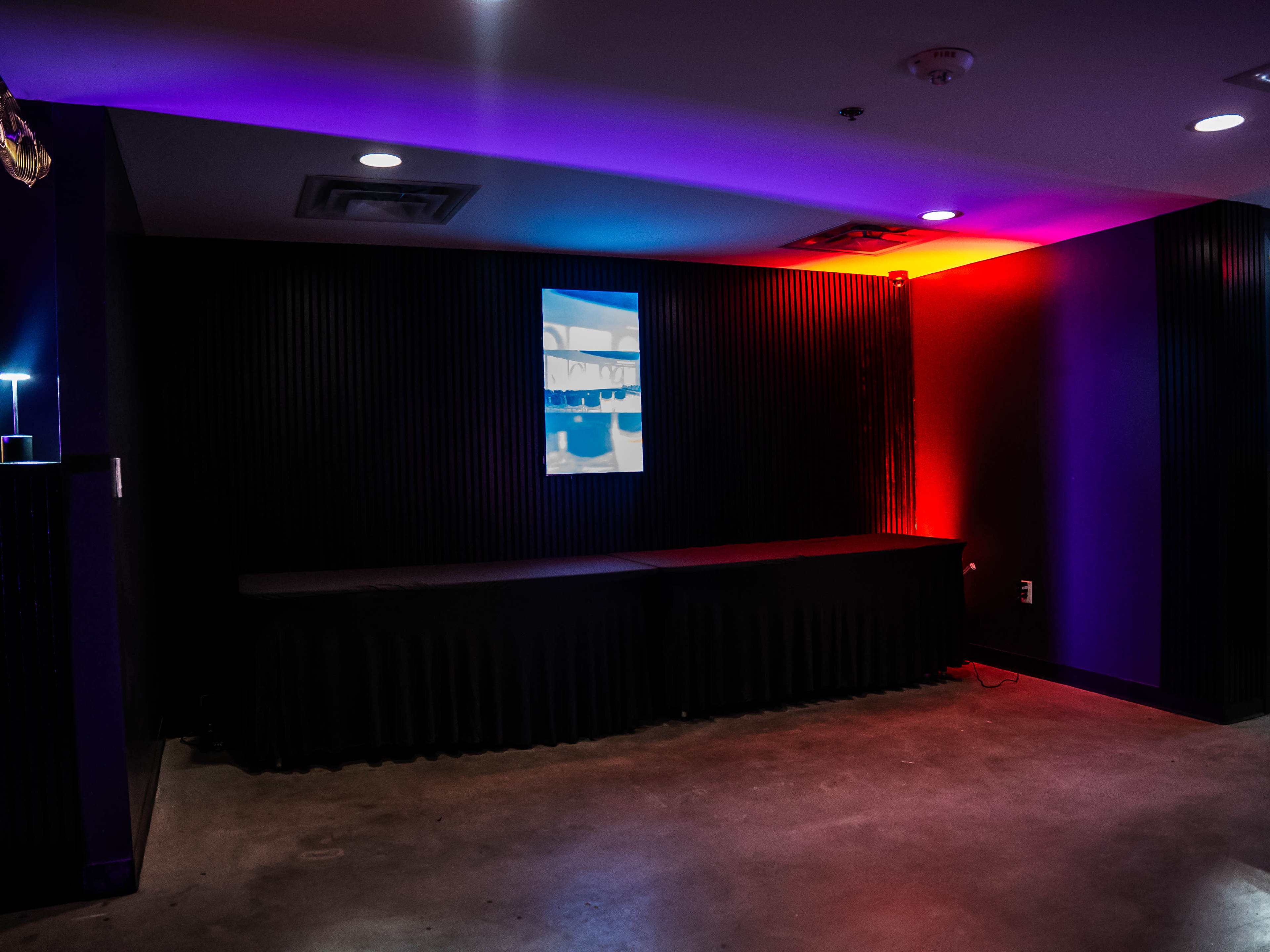 The image shows a dimly lit room with a black wall, a small screen displaying an image, and ambient lighting in purple and red hues.