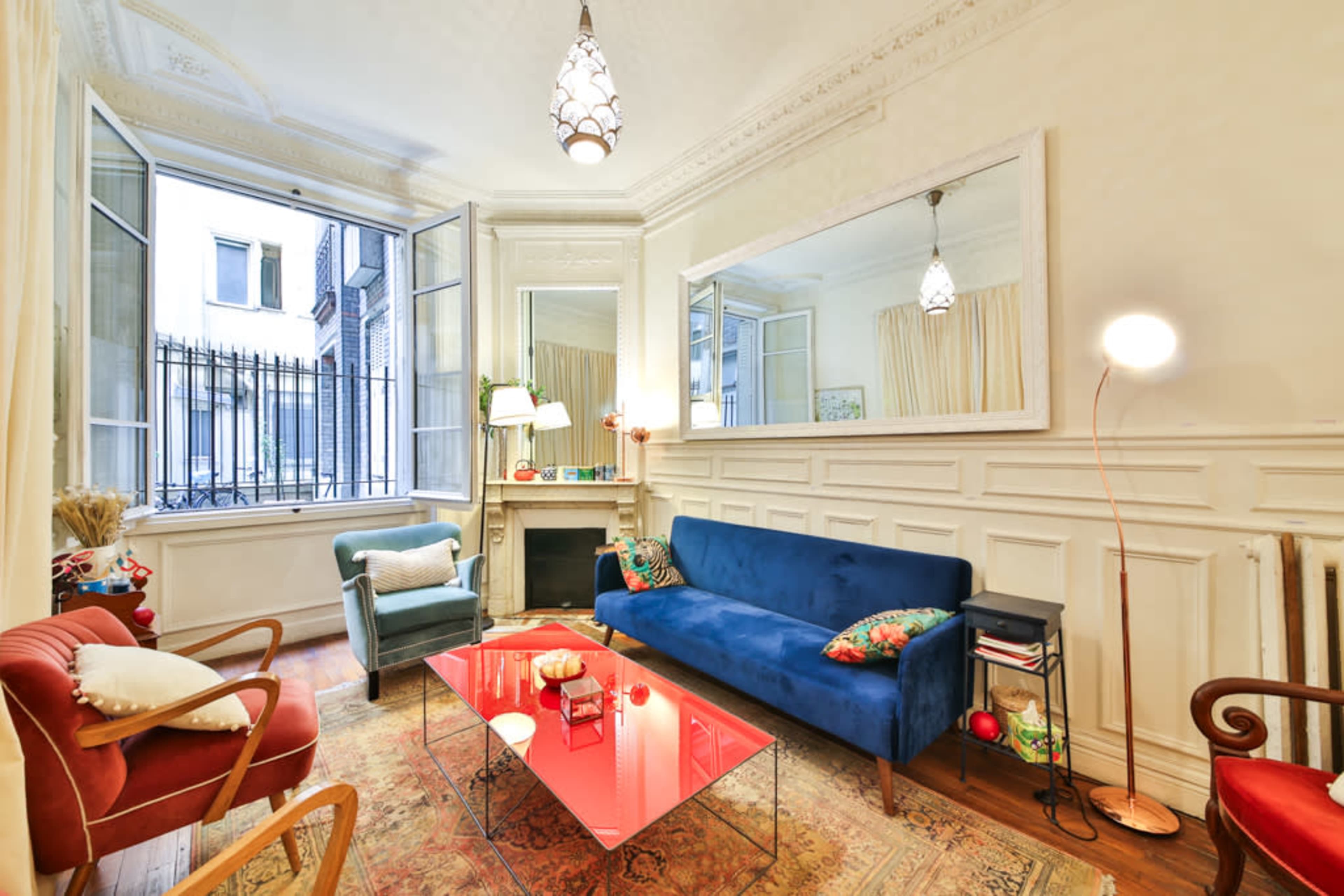 The image shows a cozy living room featuring a blue sofa, a glass coffee table, and large windows that allow natural light to flood the space.