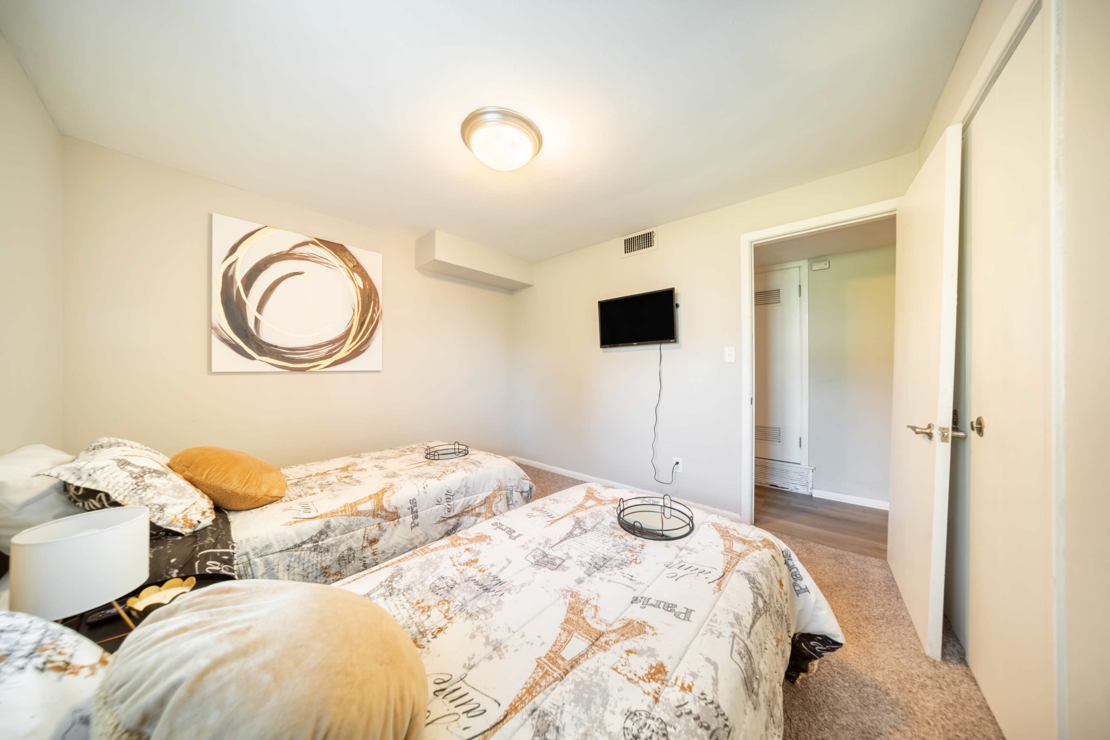 A bedroom with two twin beds, a wall-mounted TV, and a piece of abstract art on the wall.
