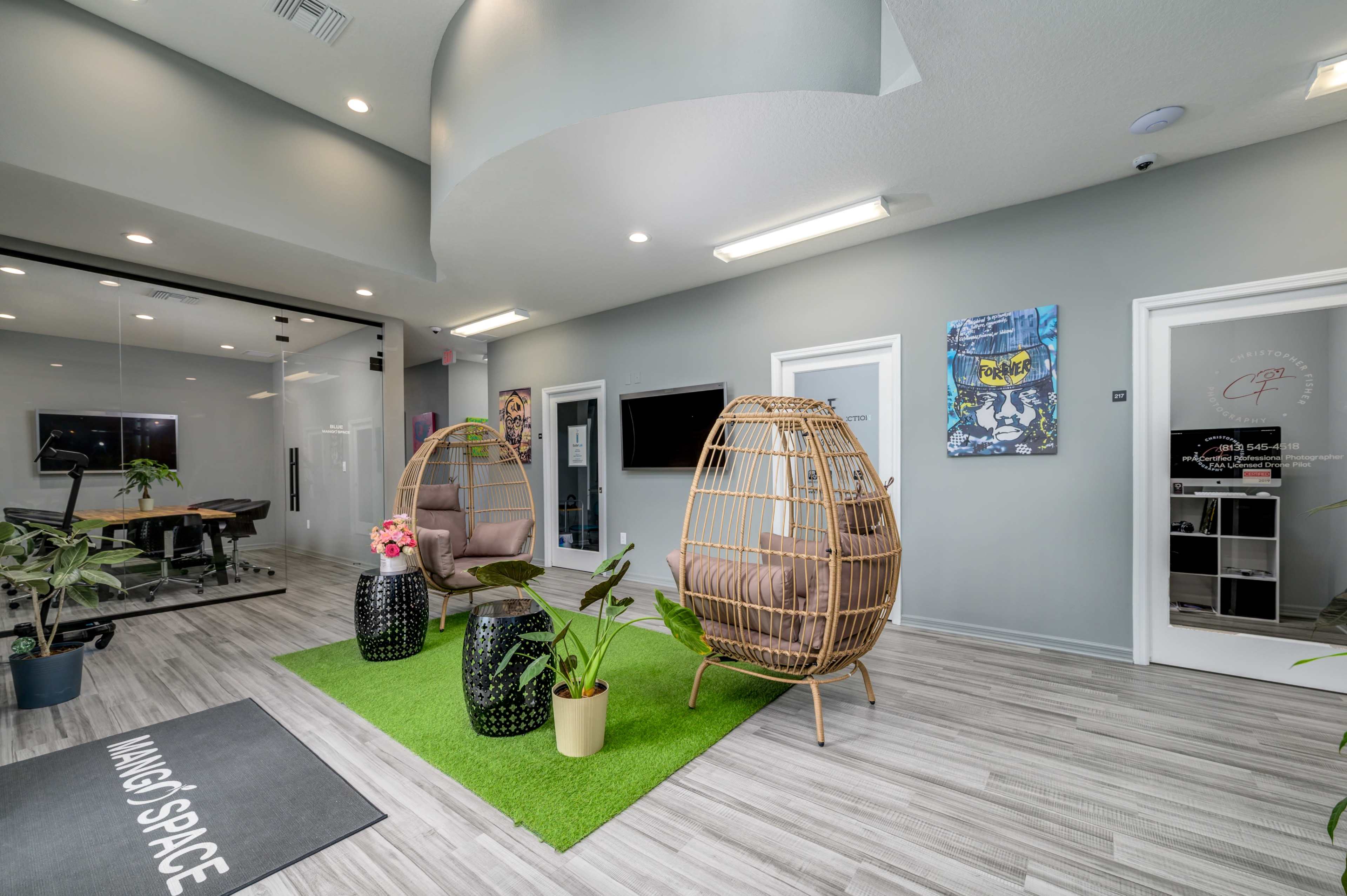 The image shows a modern reception area featuring two hanging chairs, greenery, and a light gray color scheme.