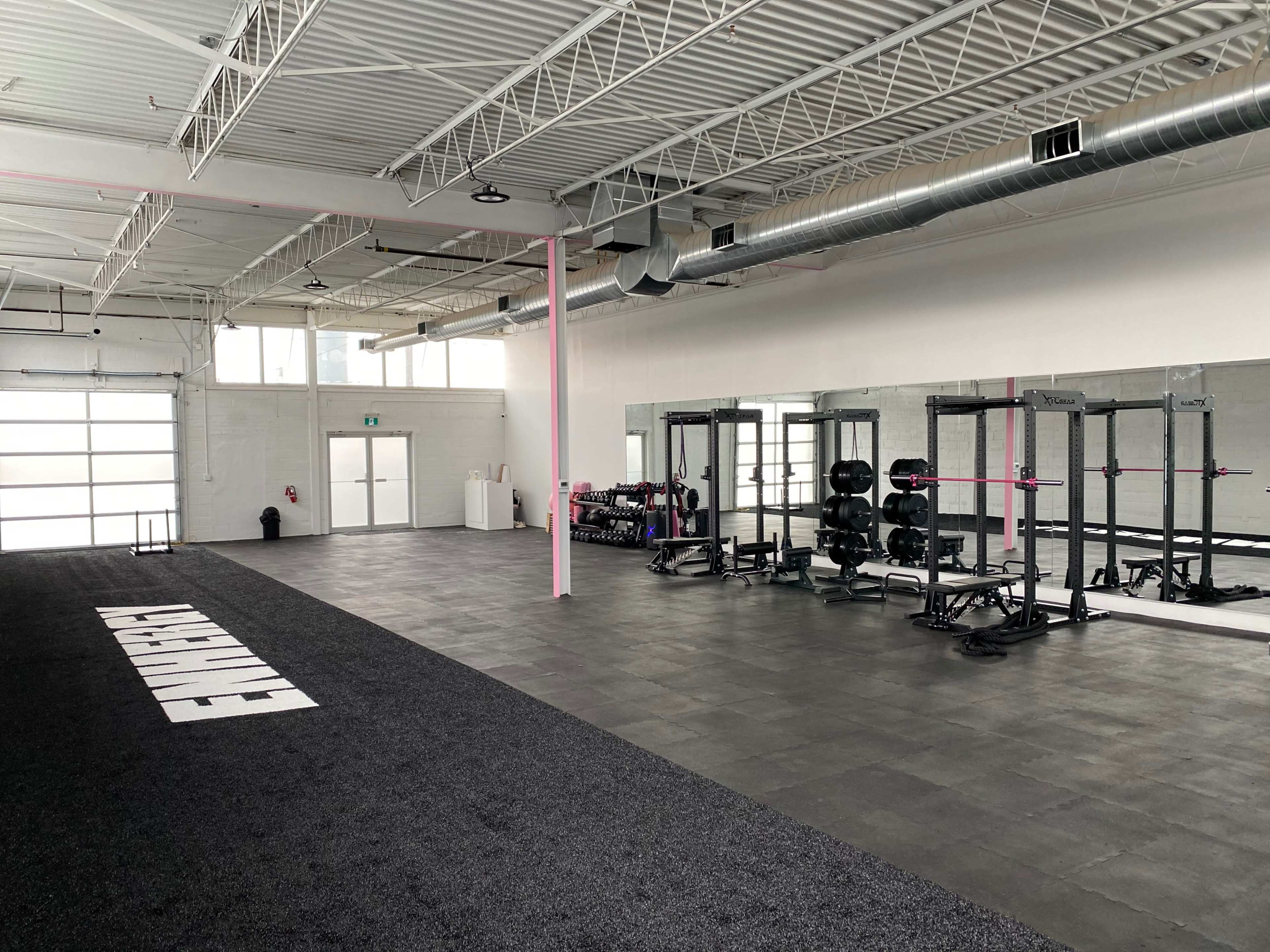 A spacious gym interior with workout equipment, mirrors, and a black rubber flooring.