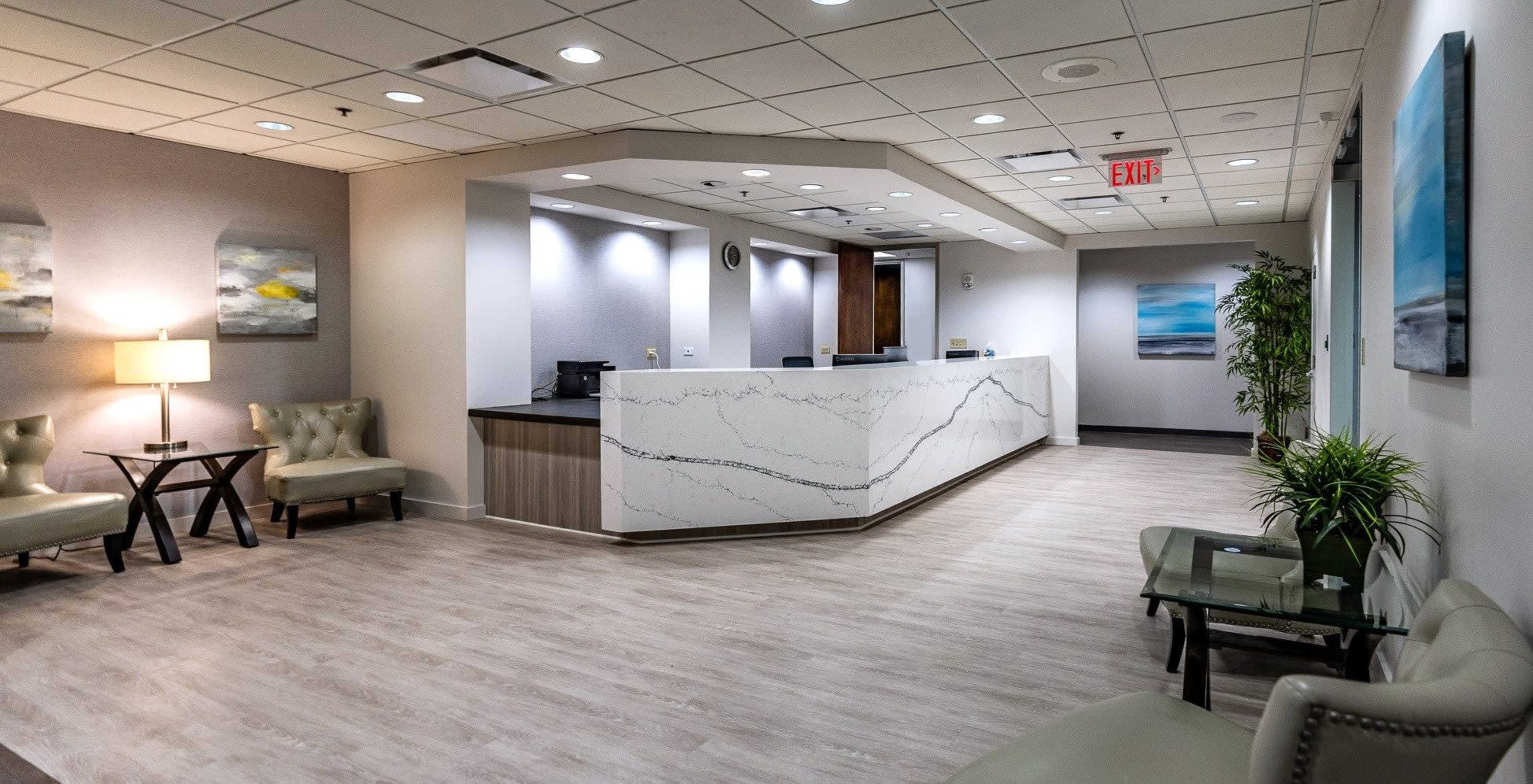 The image shows a modern reception area featuring a sleek front desk, soft seating, and decorative artwork on the walls.