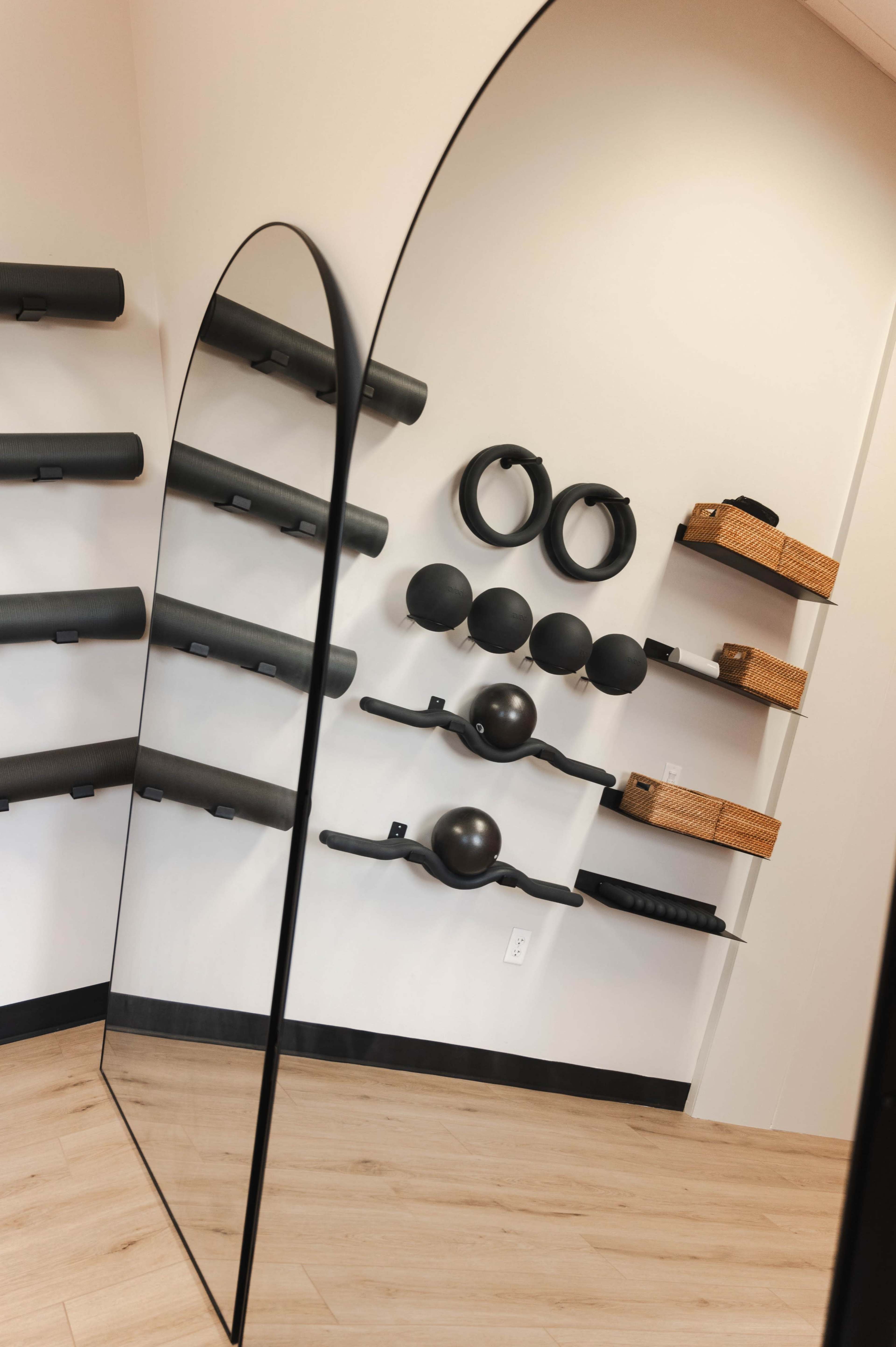 The image shows a fitness studio with a large mirror and various exercise equipment organized on the walls.