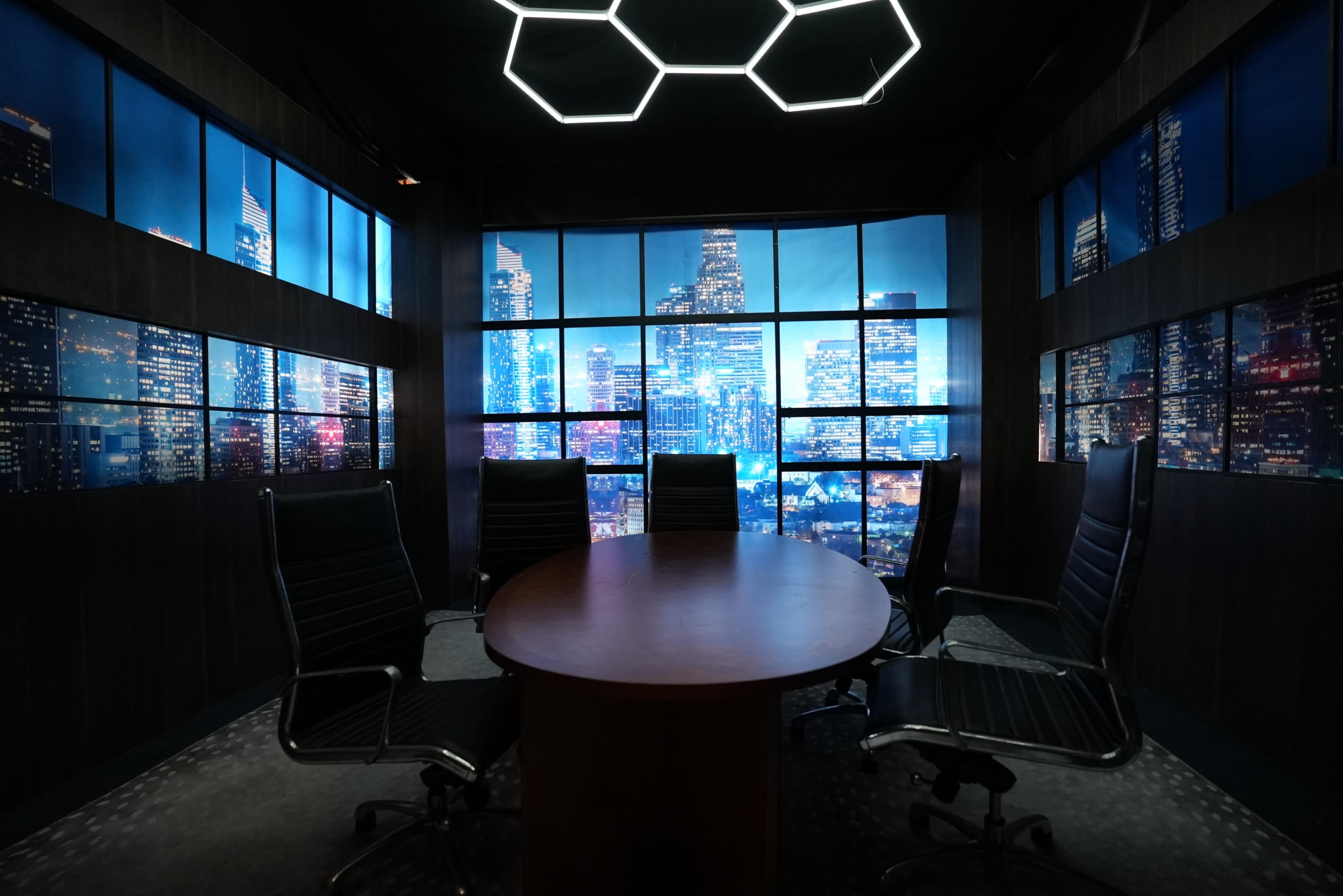 The image shows a modern conference room with a circular table and several black chairs, overlooking a city skyline illuminated at night.
