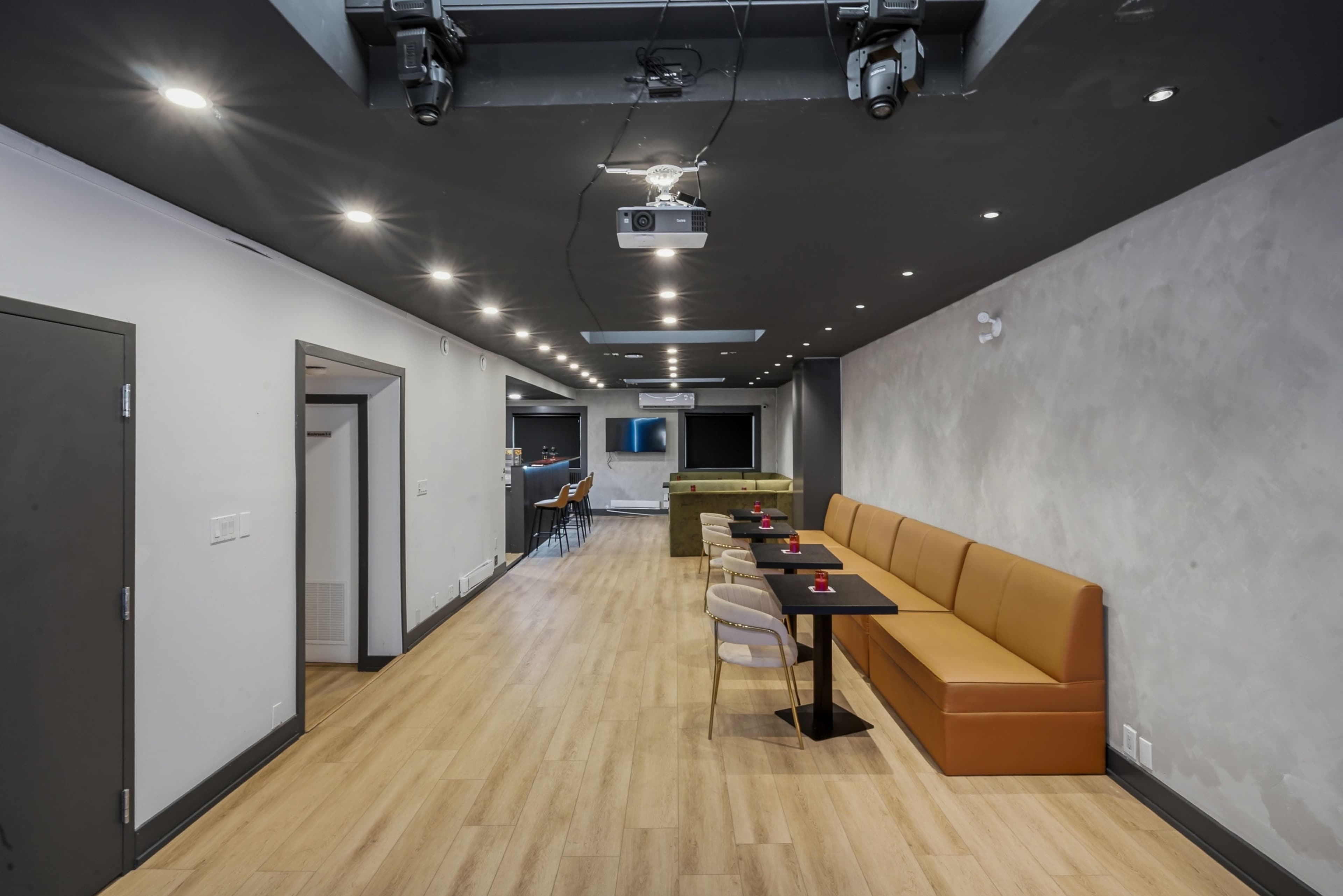 A long, modern room features a brown seating area on one side, a table, and a projection screen at the far end.