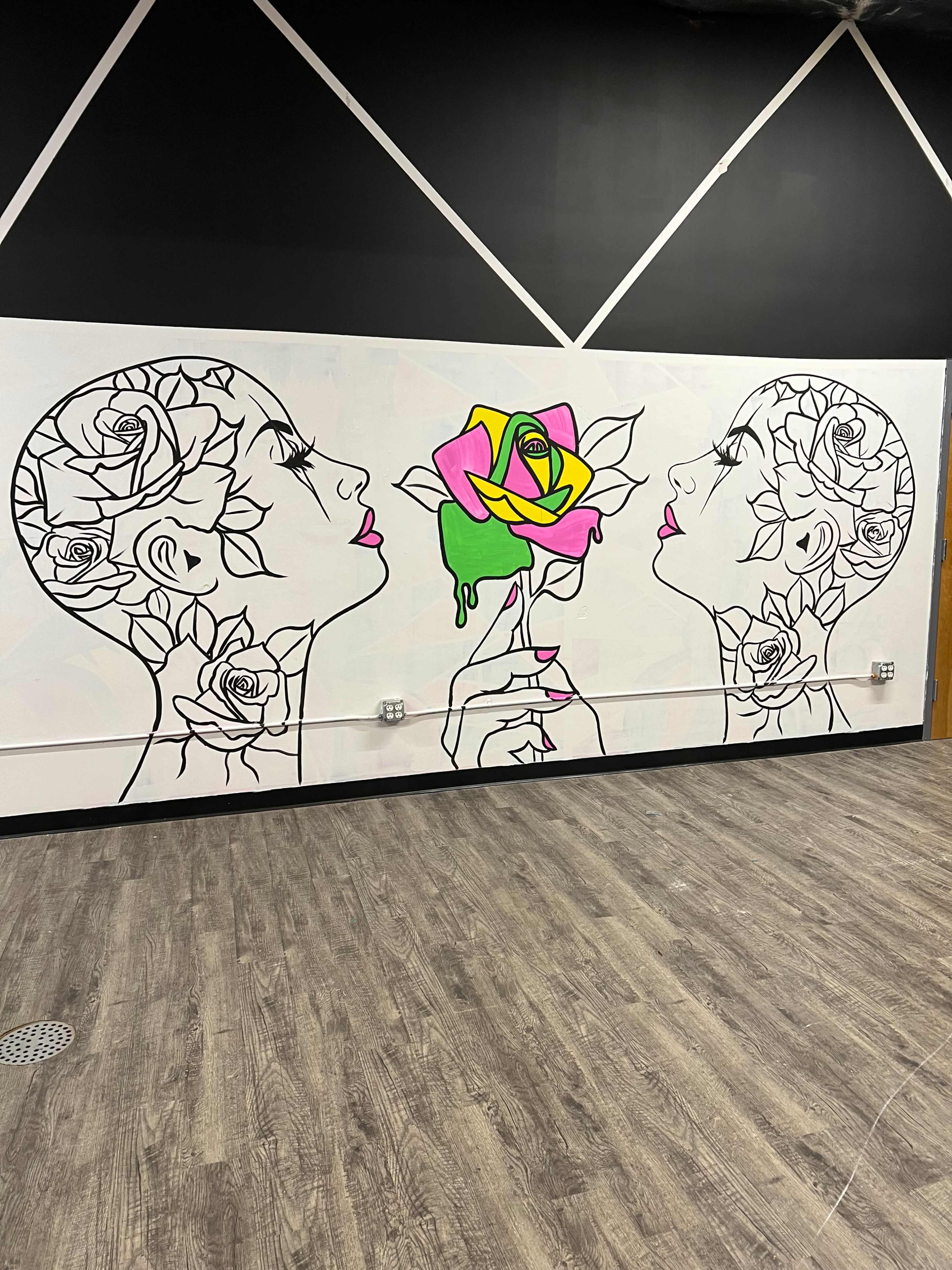 A mural featuring two outlined profile heads with floral designs and a colorful rose between them against a black wall.